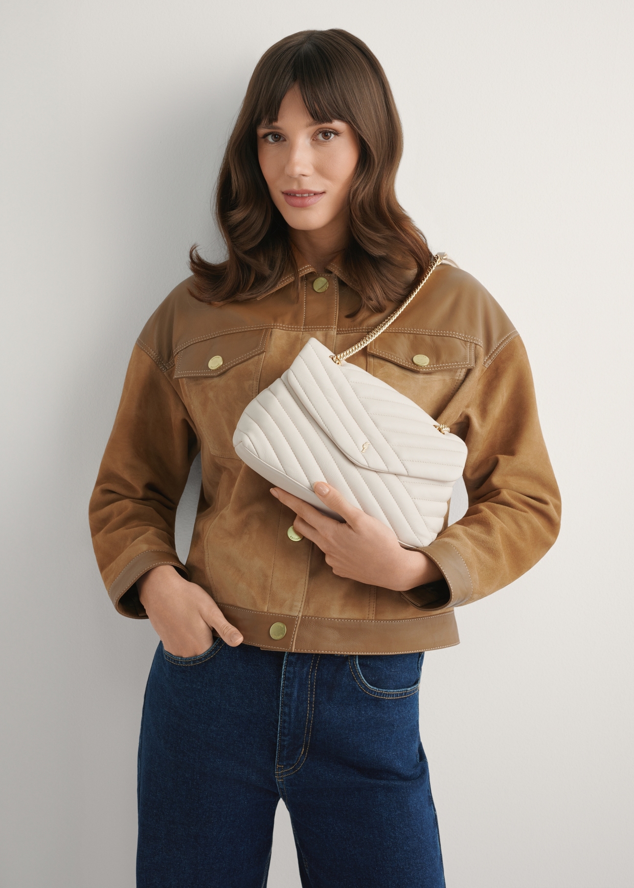 Cream-colored leather handbag TORES-1285-0B(W26) - view of the product held in the model's hand, against a light background. Half of the silhouette is visible.