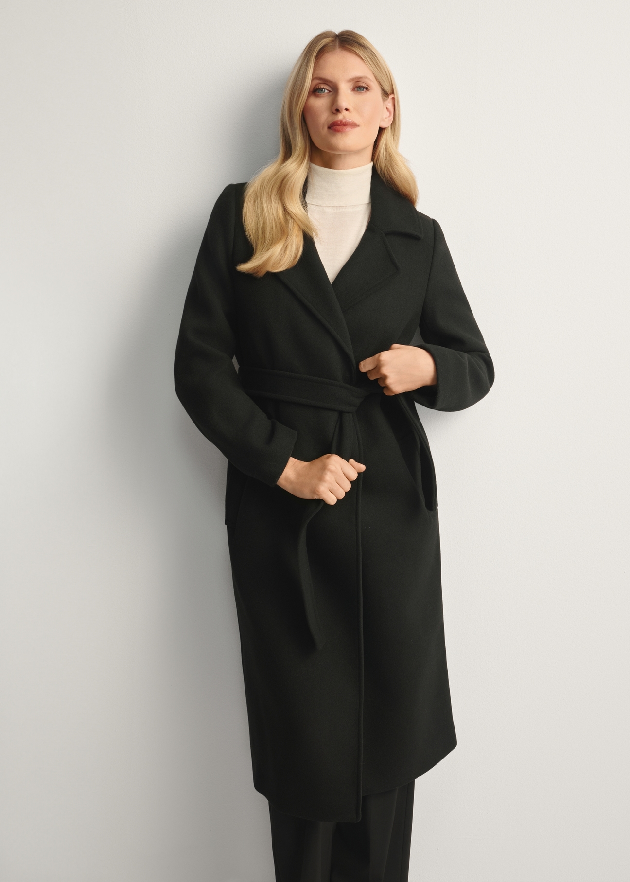 Black long women's coat PLADT-0048B-99(Z25), front view of the product on the model, half of the silhouette visible.