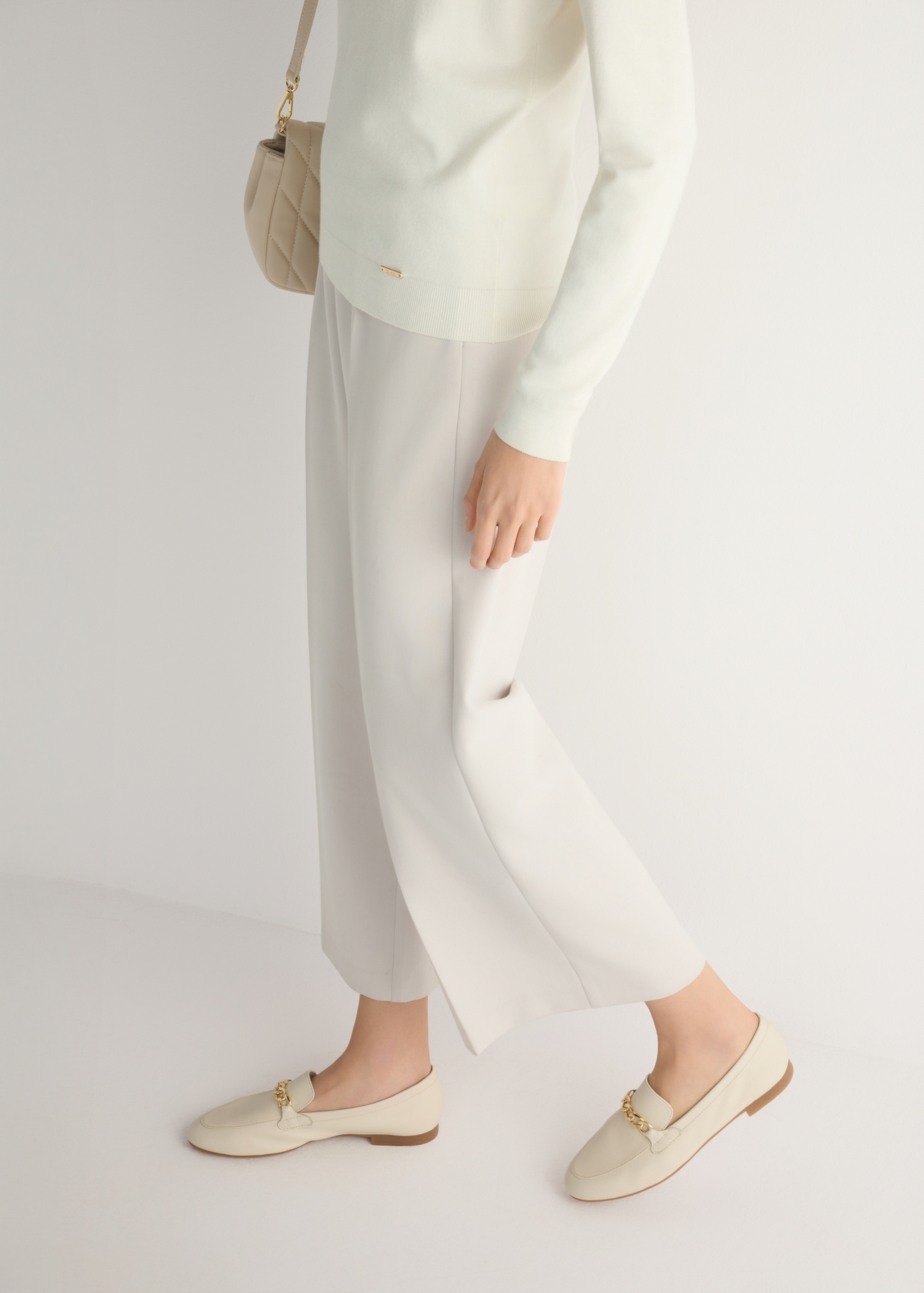 Women's cream leather moccasins with chain BUTYD-0914A-0B(W26), side view of the product on the model, half of the silhouette visible.