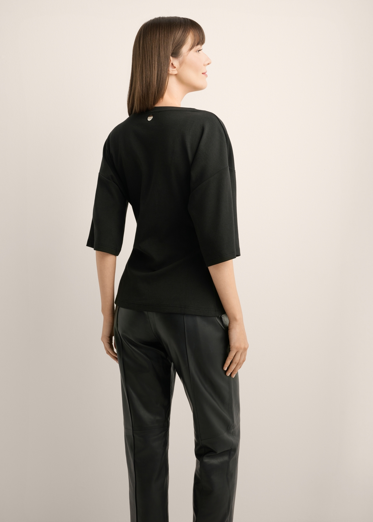 Black women's blouse with draping TSHDT-0163-99(Z26), product view from the back on the model, half of the silhouette visible.