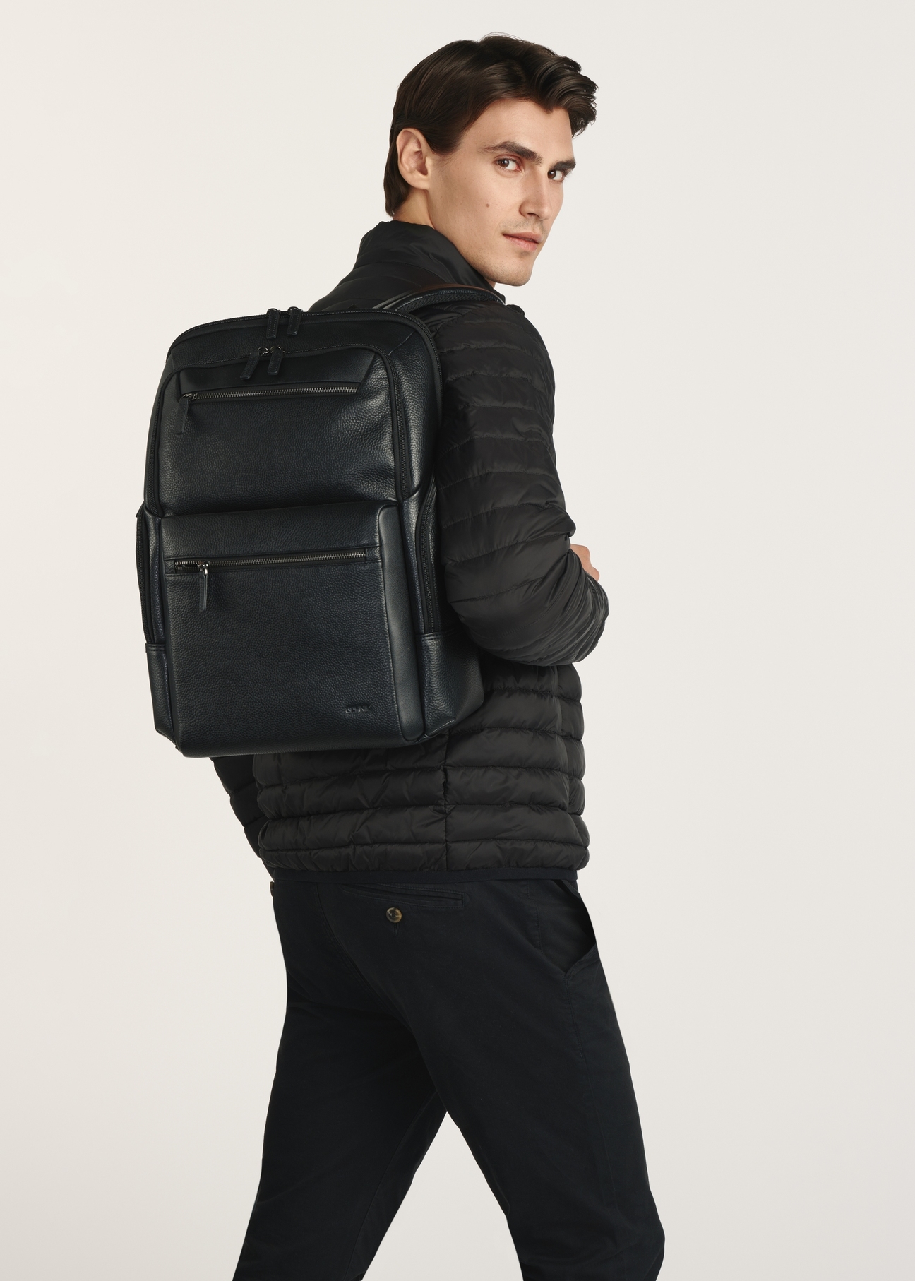 Black spacious leather backpack PLCMS-0023-99(Z25), front view of the product on the model, half of the silhouette visible.