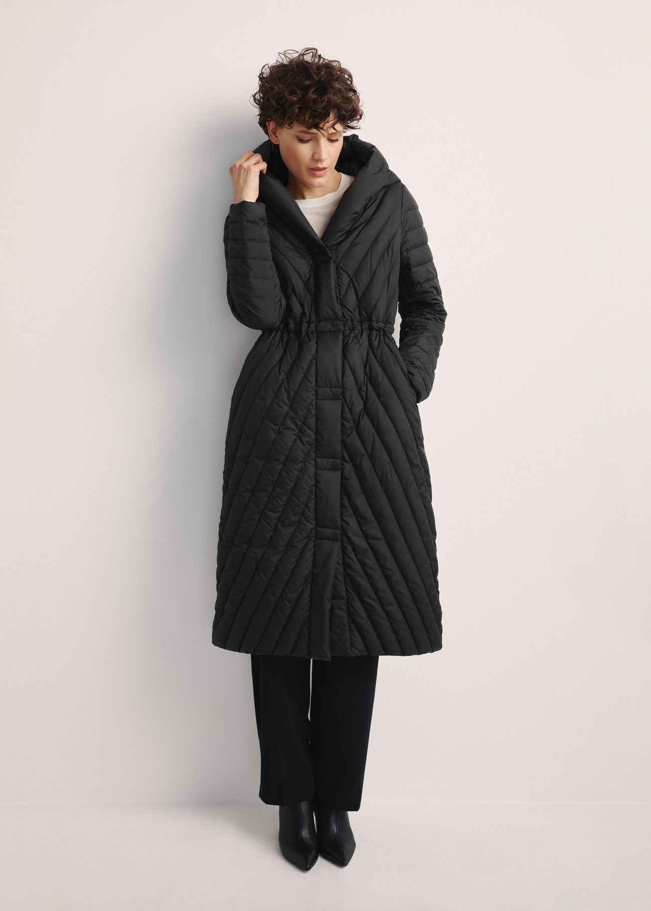 Women's long jacket with quilting KURDT-0523-98(Z25), front view of the product on the model, the entire silhouette is visible.