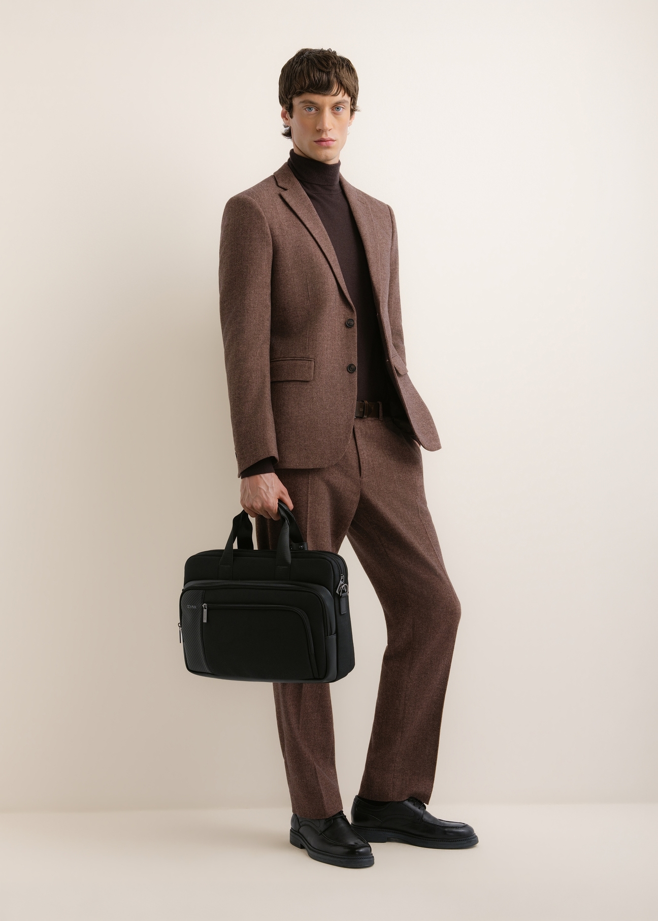 Black men's laptop bag TORMN-0443-99(Z26); front view of the product held in a model's hand, with the model's full figure visible.