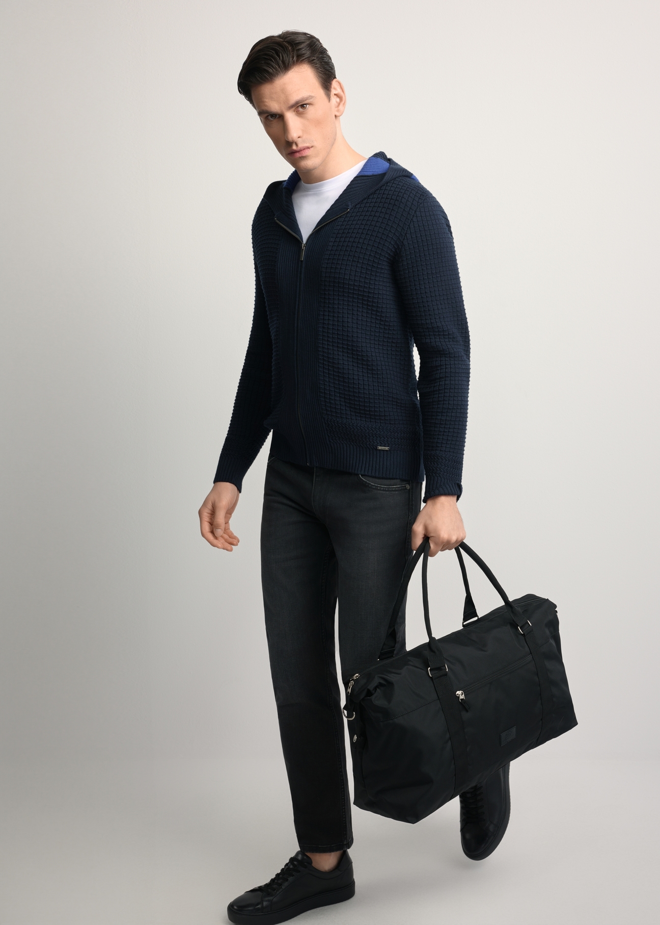 Black TORMN-0382-99(Z25) travel bag - diagonal view of the product, held by the model, against a light background. The entire silhouette is visible.