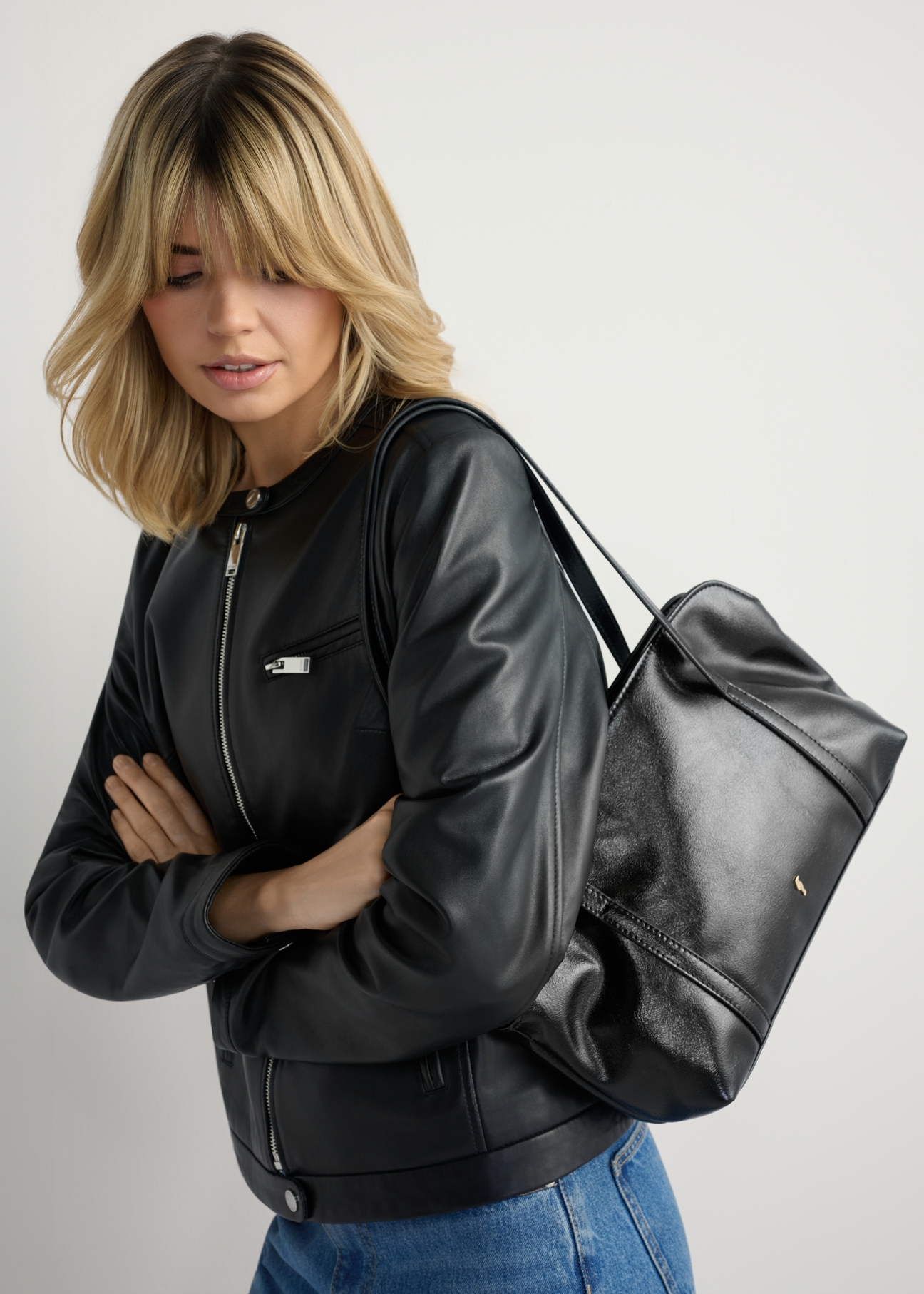 Black women's glossy handbag TOREC-1205-9F(W26) - product view slightly diagonal, on a model against a light background. Half of the silhouette visible.