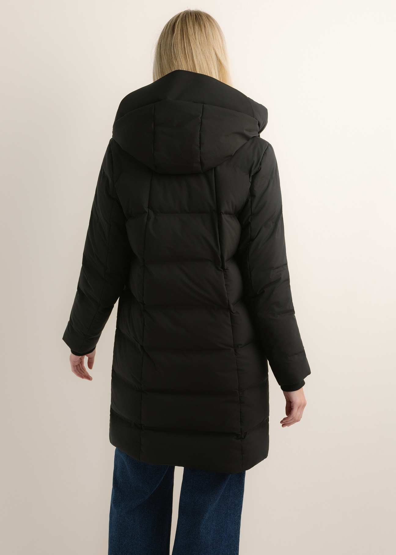Black women's winter jacket with hood KURDT-0700-99(Z26), product view from the back on the model. Half of the silhouette visible.