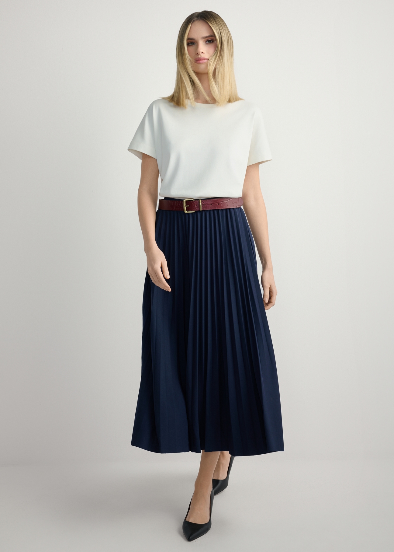 Navy blue pleated midi skirt SPCDT-0096-7E(W26), front view of the product on the model. Full body visible.
