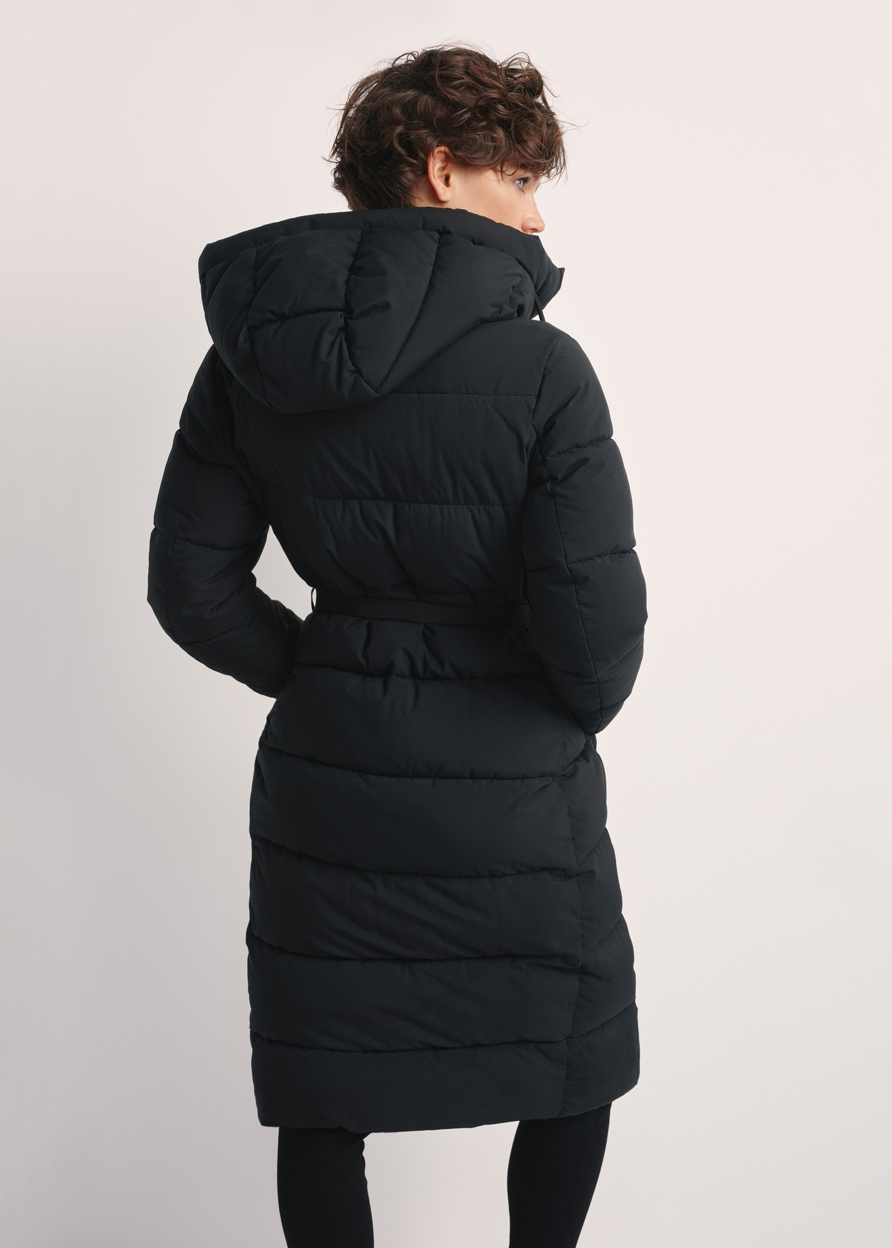 Long black women's jacket KURDT-0602-99(Z25), product view from the back on the model. Half of the silhouette visible.