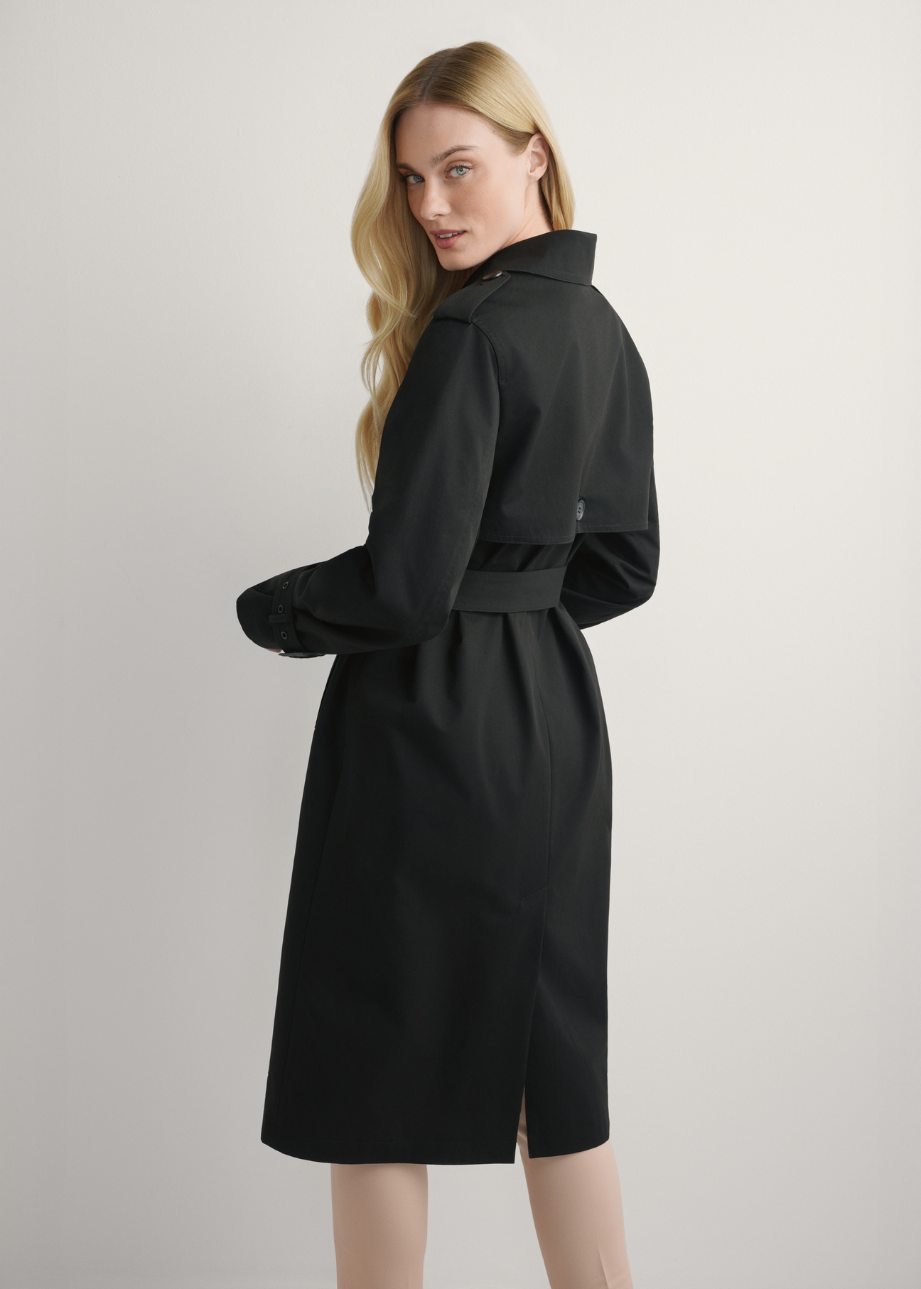 Long black women's jacket in the form of a coat KURDT-0512-99(W25), product view from the back on the model, half of the silhouette visible.