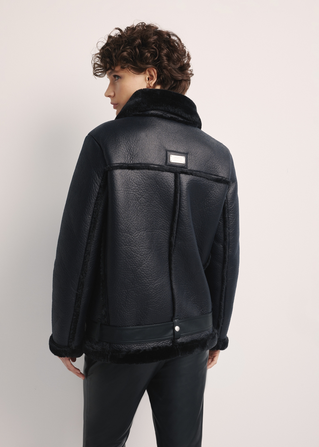 Black short women's sheepskin coat KOZDP-0001A-99(Z24), product view from the back on the model, half of the silhouette visible.