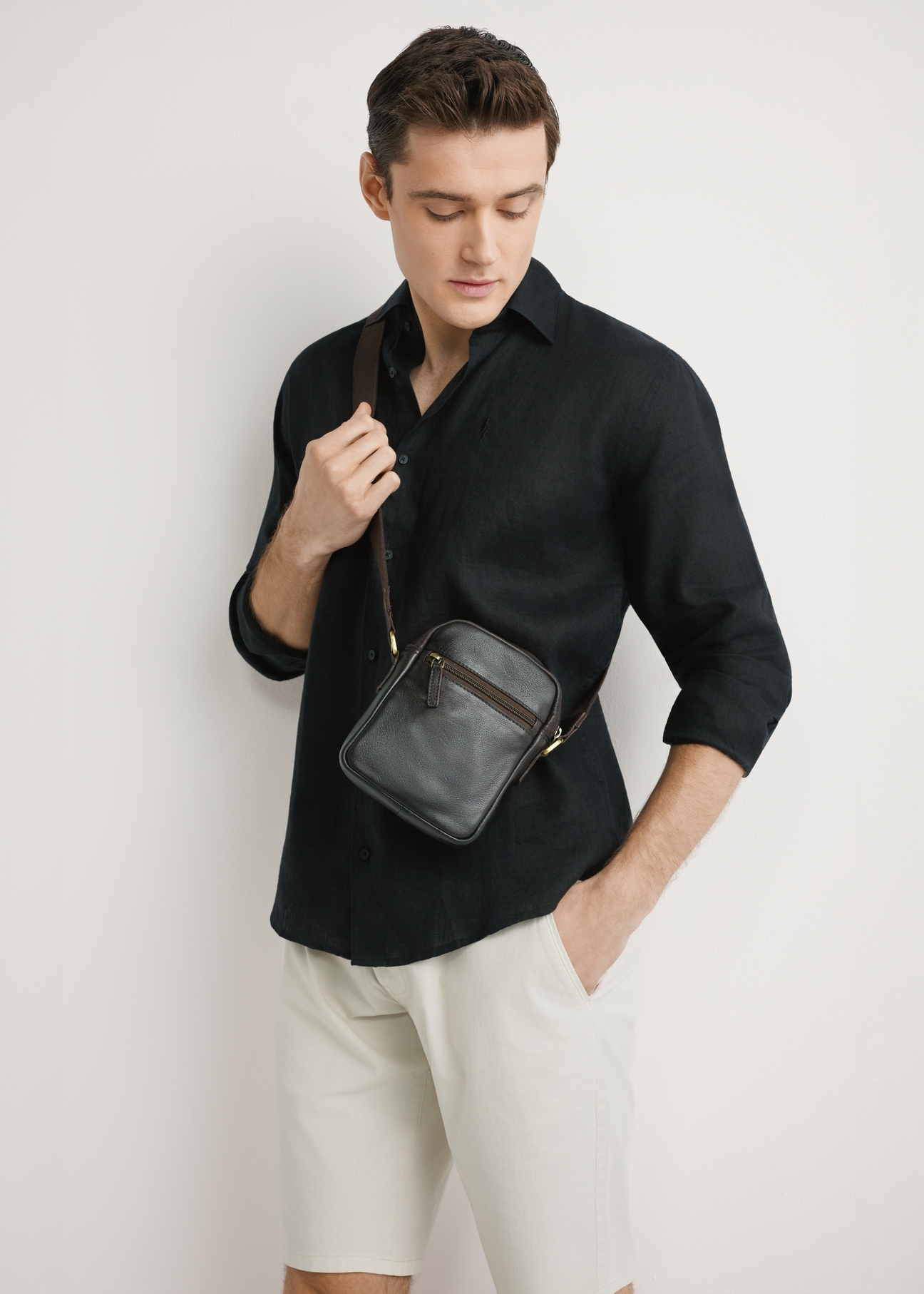 Ciemnobrązowa skórzana saszetka męska TORMS-0501-1I(W26) - widok produktu z przpodu, na modelu, na jasnym tle. Widoczna sylwetka do kolan.