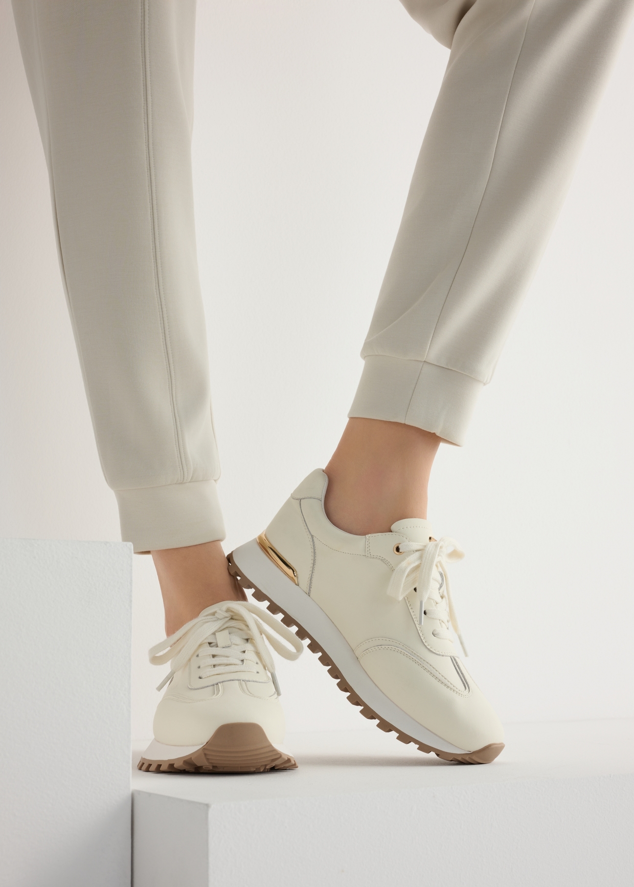 Women's leather sneakers in cream color BUTYD-1270-0B(W26), side view of the product on the model, half of the silhouette visible.