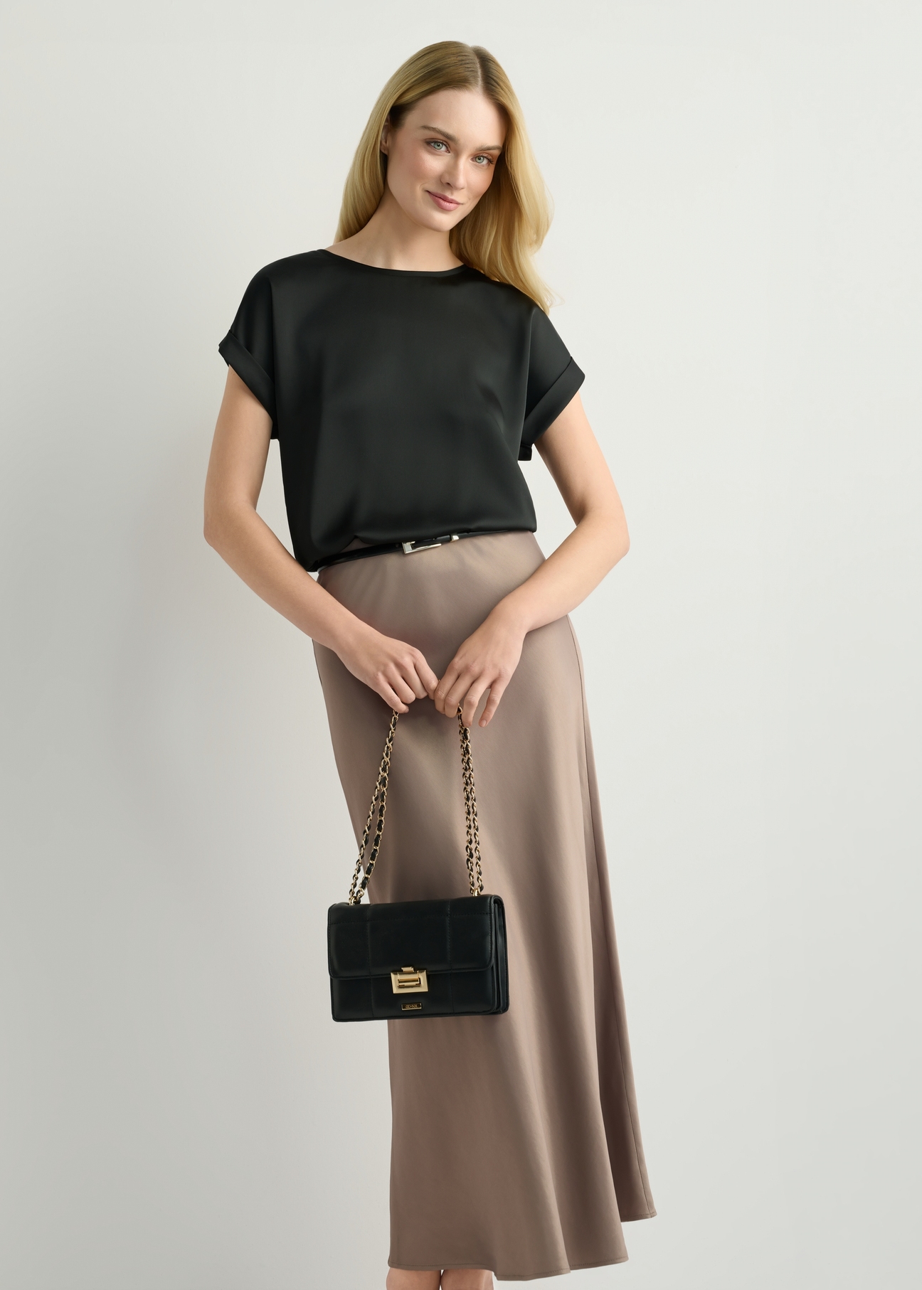 Small black women's handbag TOREC-1186-99(W26) - front view of the product, held by the model, against a light background. The entire silhouette is visible.