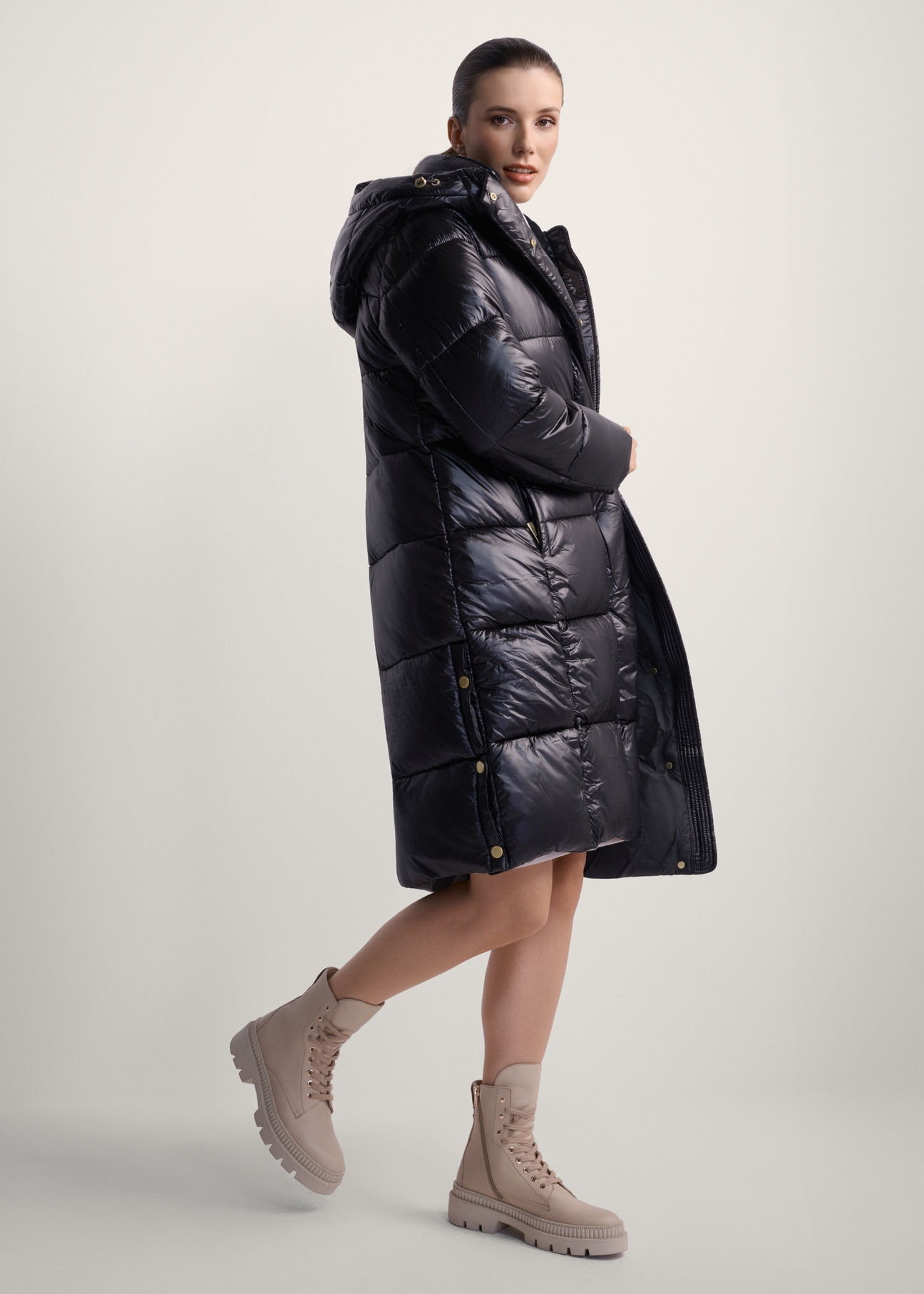 Black long women's winter jacket KURDT-0531A-99(Z25), product view from the side on the model, the whole silhouette is visible.