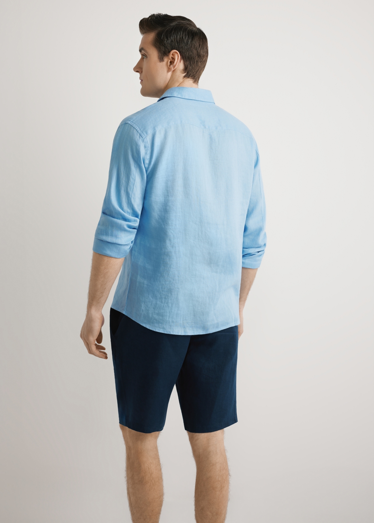 Modrá pánska ľanová košeľa KOSMT-0321A-7B(W26), pohľad zozadu na výrobok, na modelke, na svetlom pozadí. Viditeľná polovica siluety.