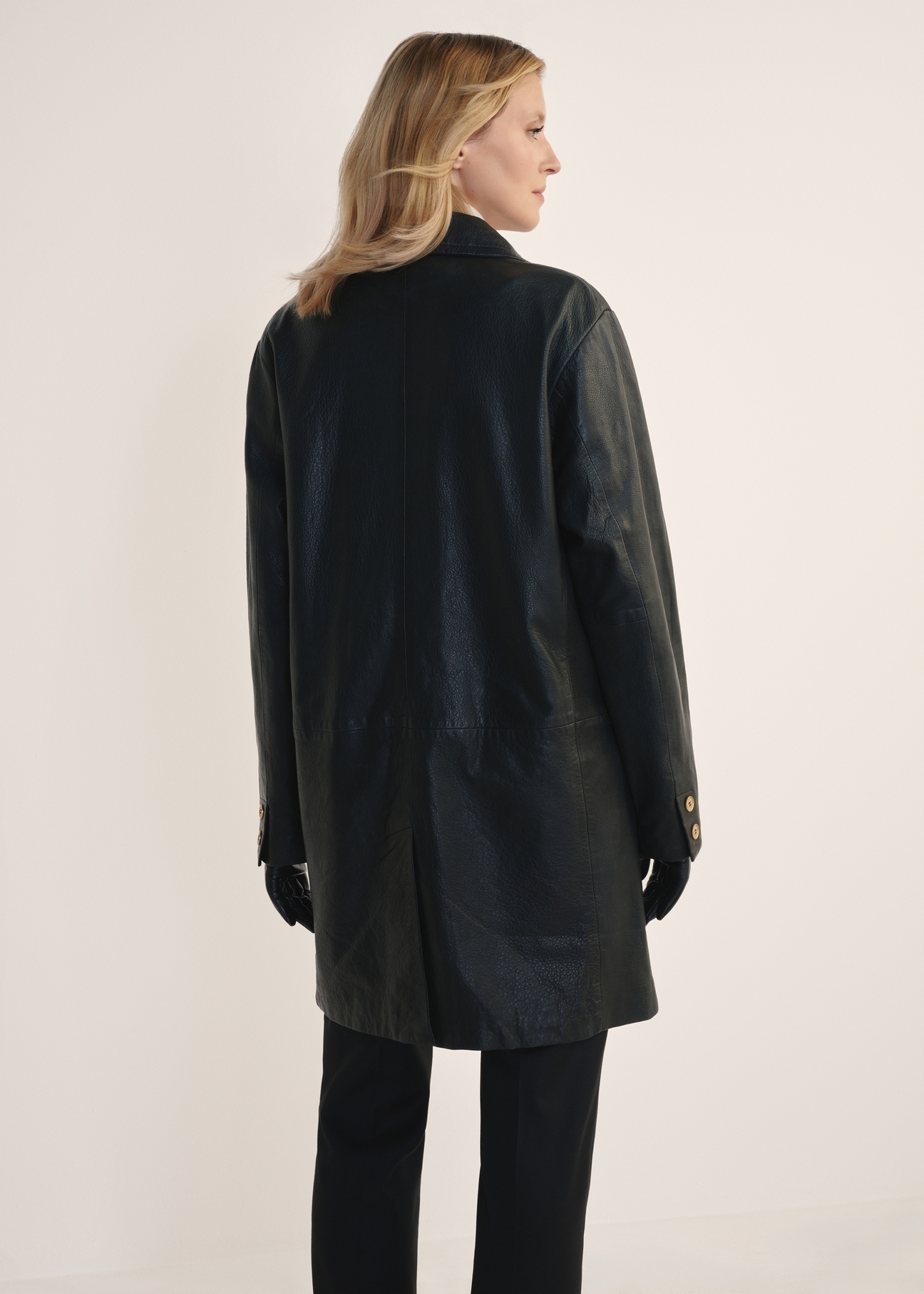 Women's leather jacket in the form of a coat KURDS-0443-1313(Z25), view of the product from the back on the model, half of the silhouette visible.