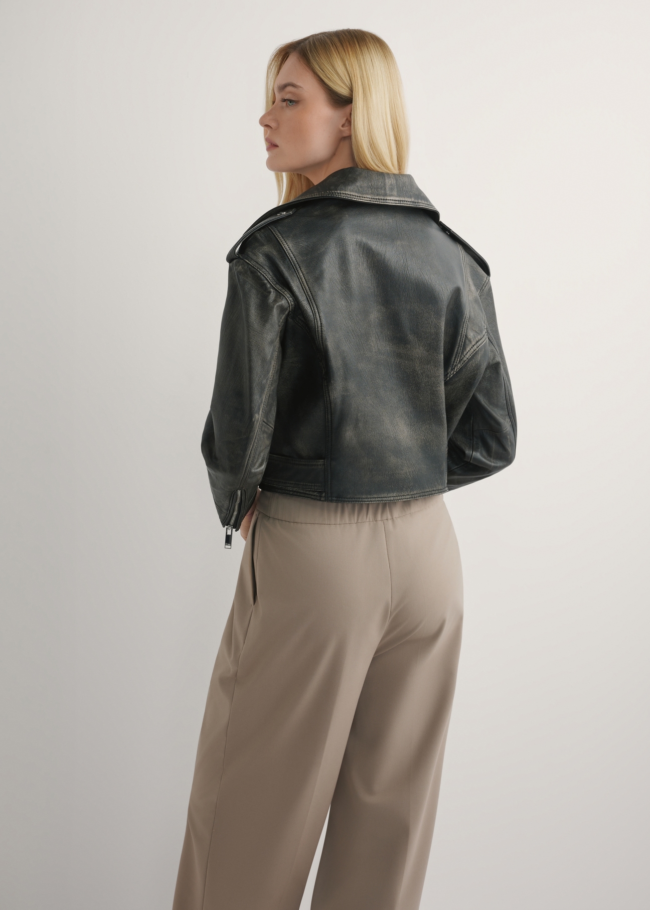 Women's short leather biker jacket KURDS-0434-99(W26) - back view of the product, on a model, against a light background. Knee-length silhouette visible.