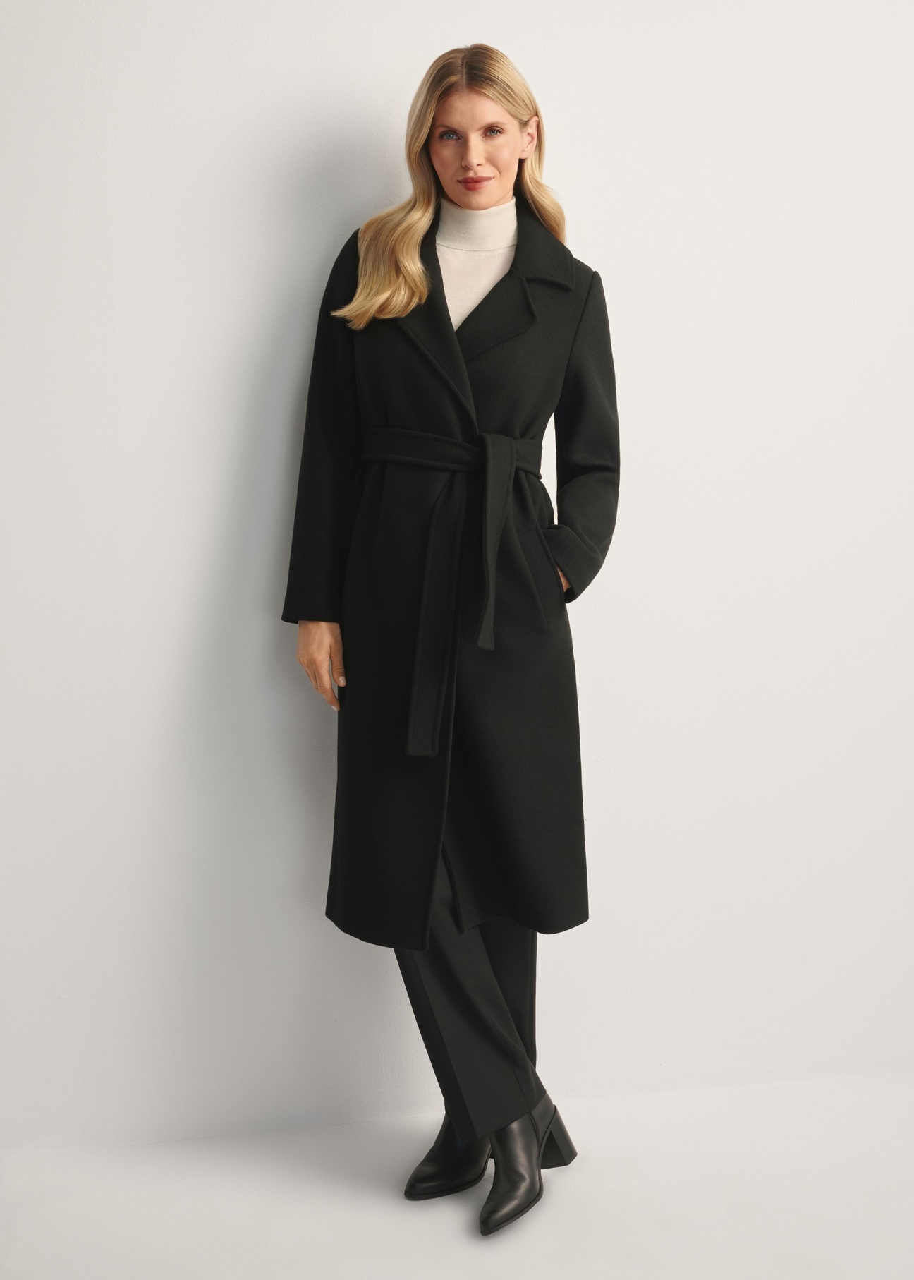 Black long women's coat PLADT-0048B-99(Z25), front view of the product on the model, the entire silhouette is visible.