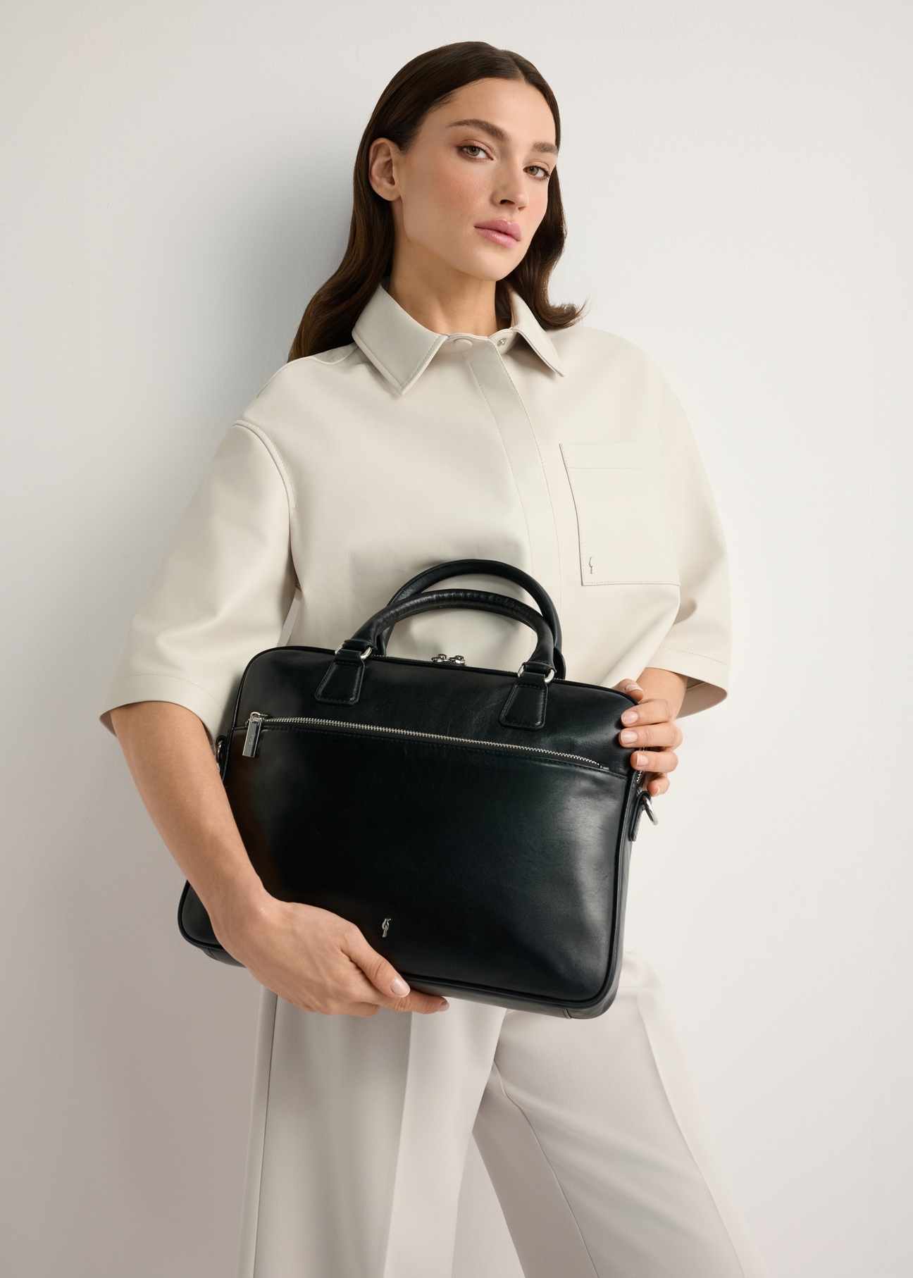 Black leather laptop bag TORES-1227-99(W26), product view in model's hands. Half of silhouette visible.