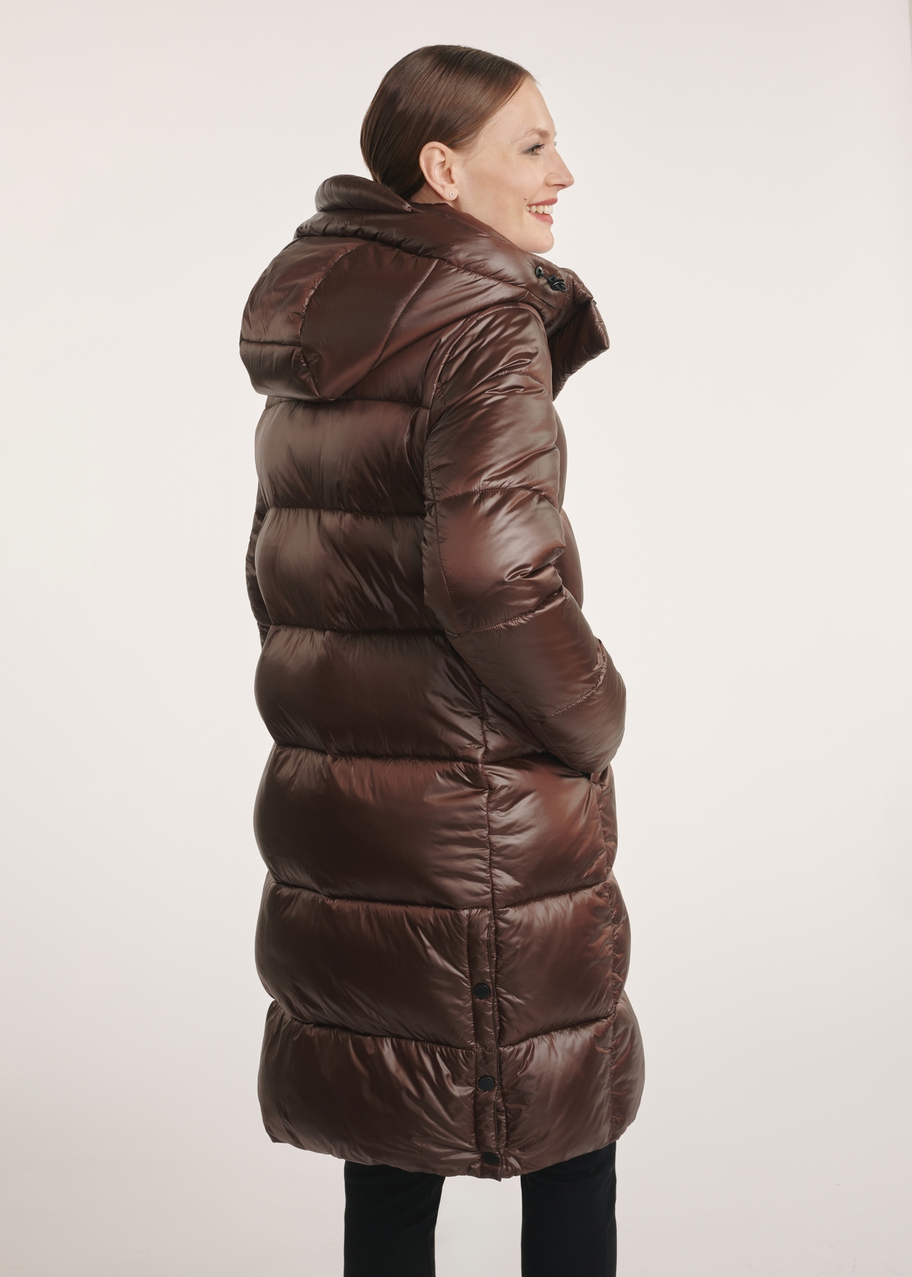 Brown long winter women's jacket KURDT-0531-89(Z25) - side view of the product on a model on a white background. Half of the silhouette visible.