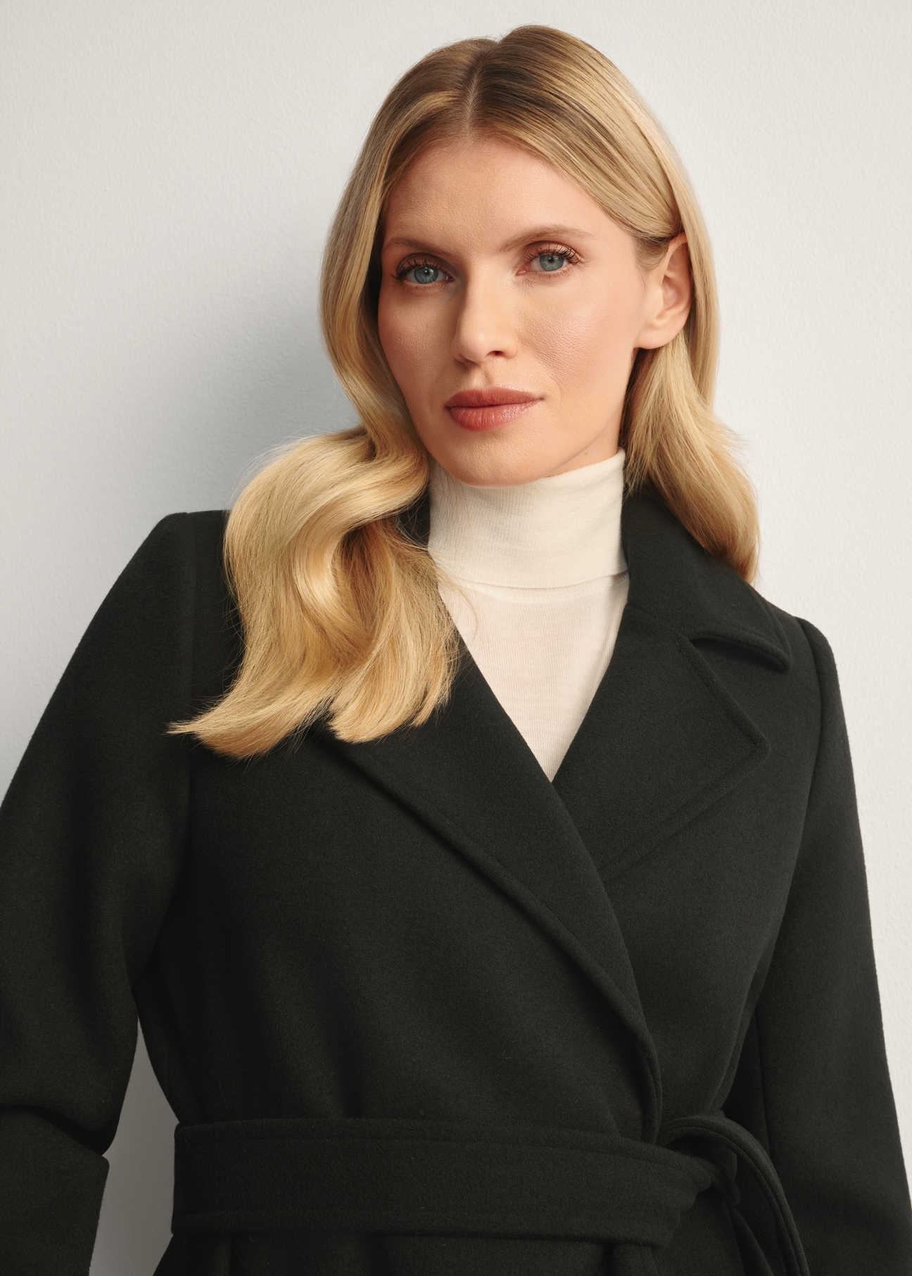 Black long women's coat PLADT-0048B-99(Z25), front view of the product on the model, close-up of the model's torso.