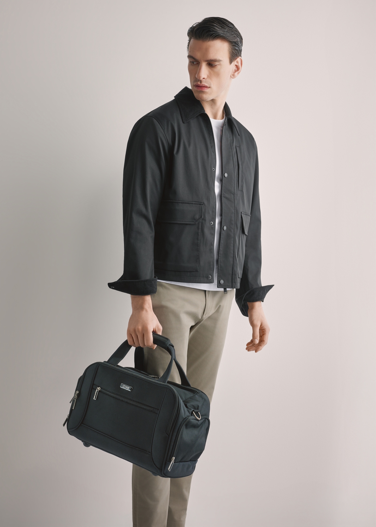 Black men's nylon bag TORMN-0420-99(W26), product view in model's hand, against a light background. Half of the silhouette visible.