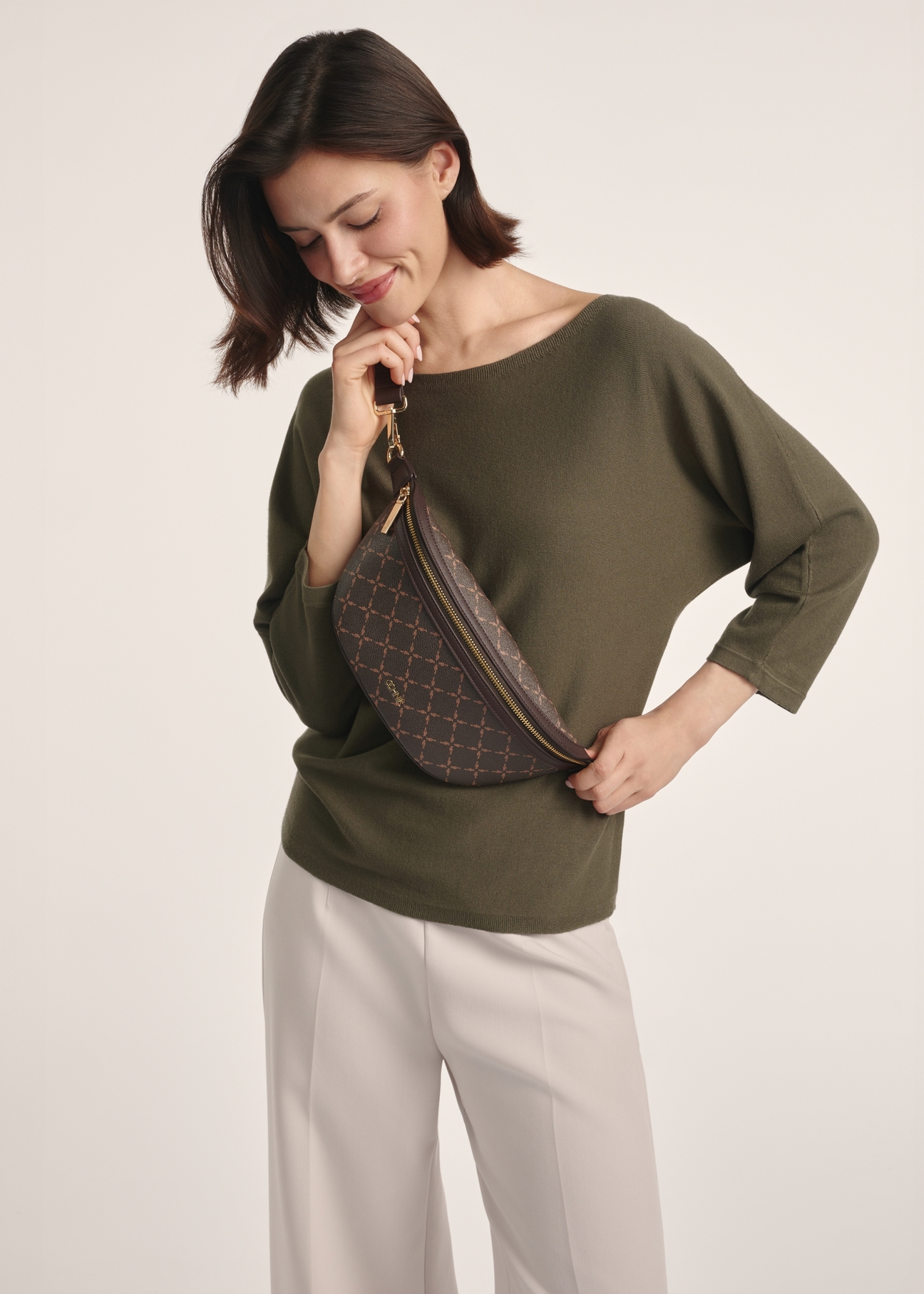 Brown waist bag with monogram TOREC-0981A-89 (Z25), front view of the product on a model, half of the silhouette visible.