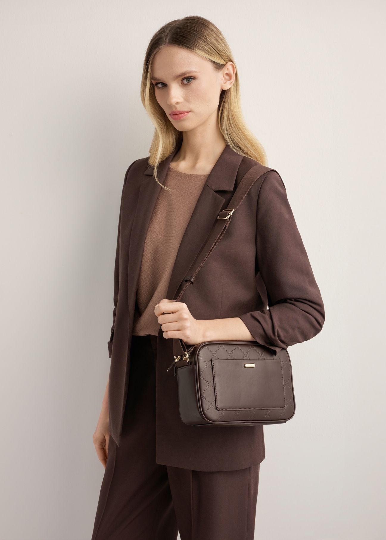 Brown women's handbag with monogram TOREC-1290-1I(Z26), diagonal view of the product on the model. Half of the silhouette visible.