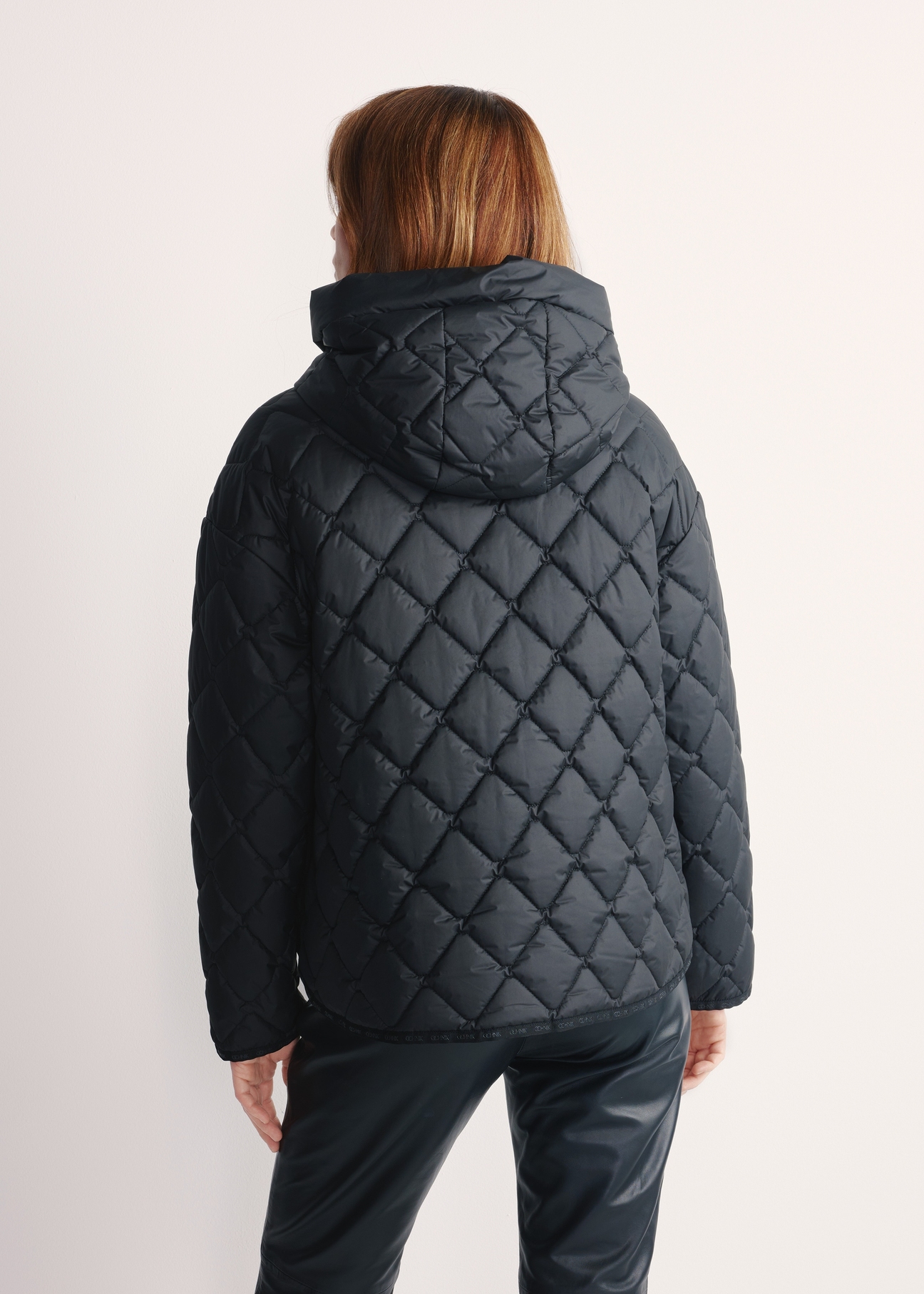 Black women's quilted jacket with hood KURDT-0588-99(Z25), back view of the product on a model, half of the silhouette visible.