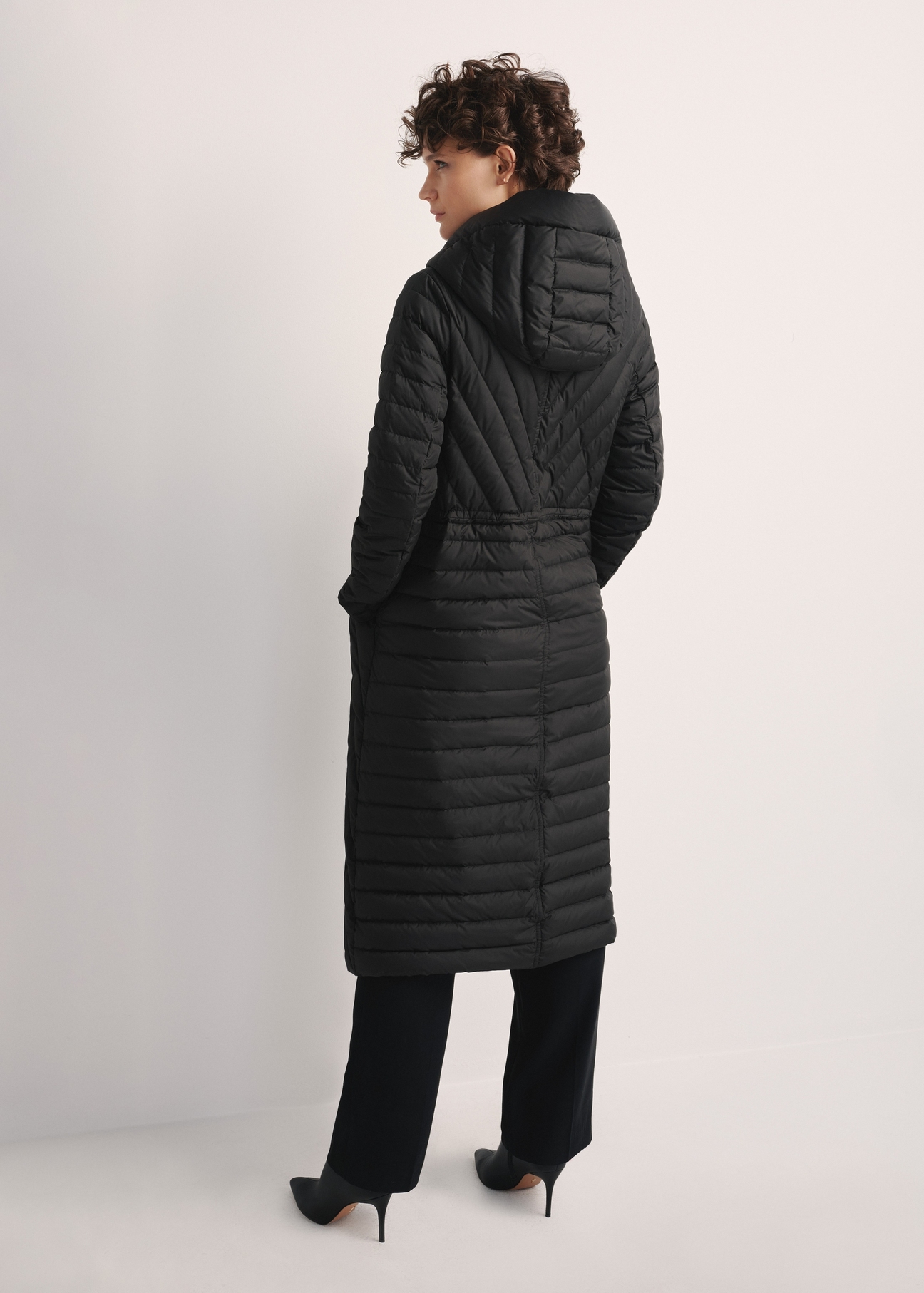 Women's long jacket with quilting KURDT-0523-98(Z25), product view from the back on the model, the whole silhouette is visible.