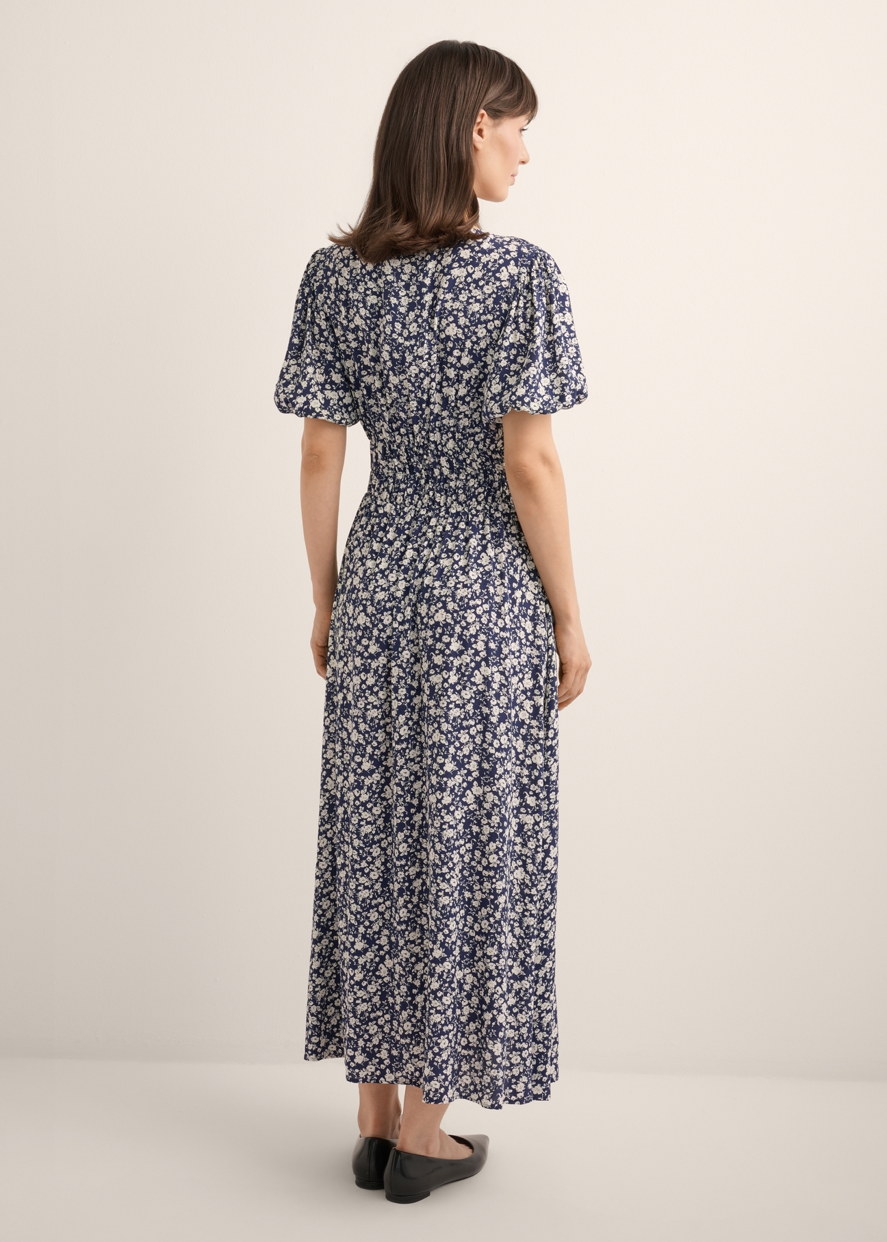 Long floral dress in navy blue SUKDT-0191-7I(W26), back view of the product on the model. Full body visible.