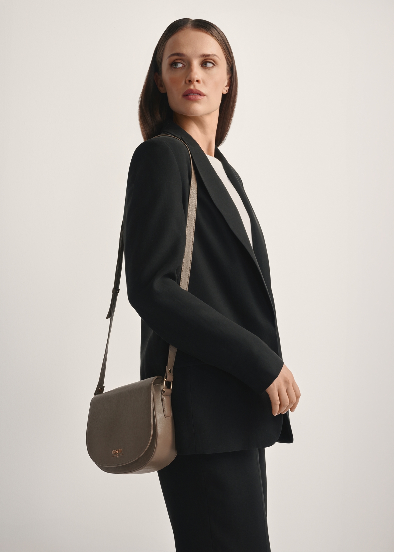 Dark beige leather semi-circular messenger bag TORES-0972F-1K(W26), diagonal view of the product on the model, half of the silhouette visible.