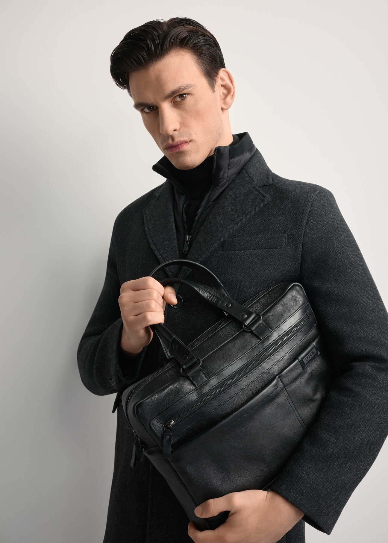 Large black leather men's briefcase TORMS-0416A-99(Z25) - front view of the product, held by the model, against a white background. Half of the silhouette visible.