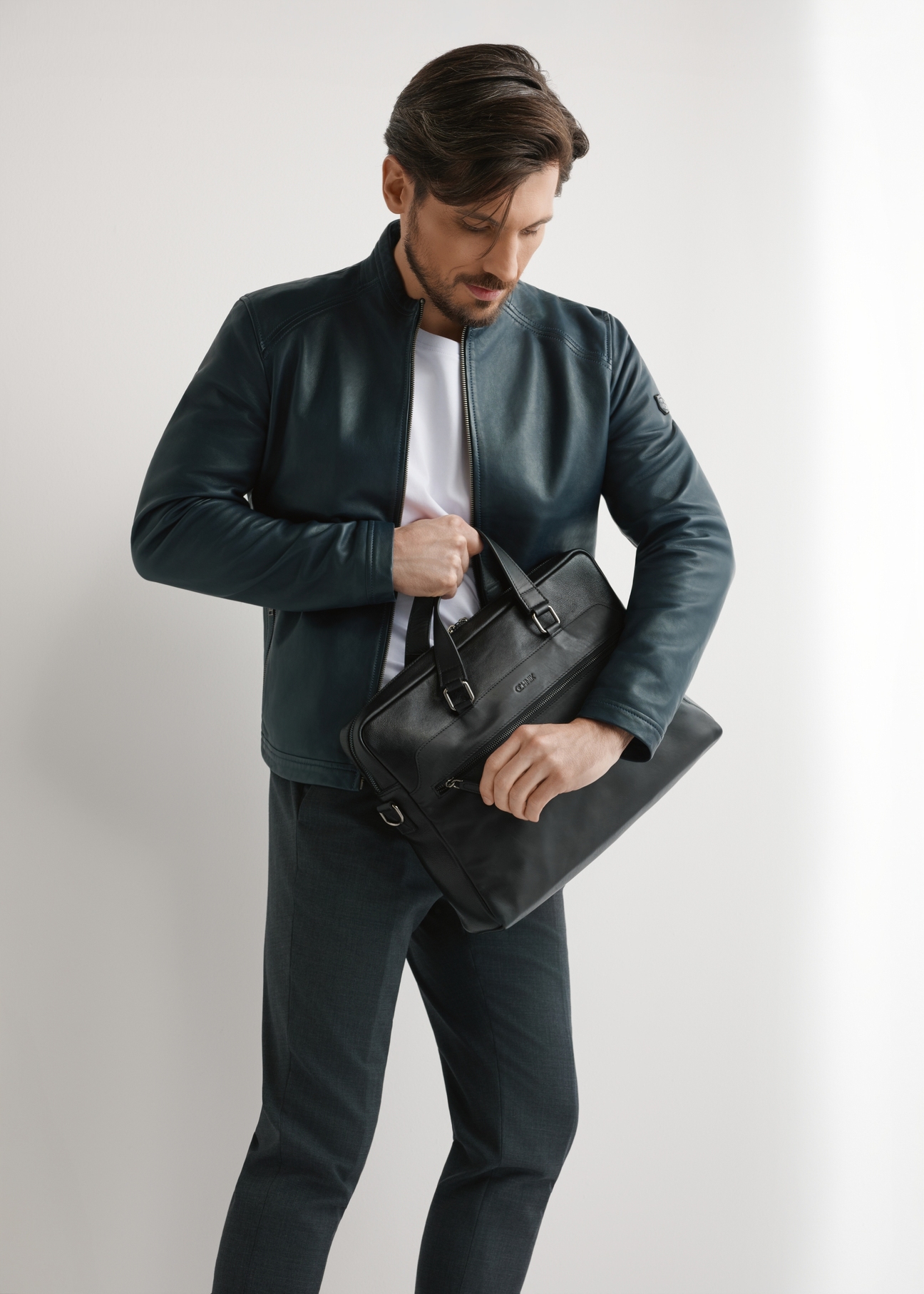 Black leather laptop bag TORMS-0496-99(W26) - diagonal view of the product, held by the model, against a light background. The entire silhouette is visible.