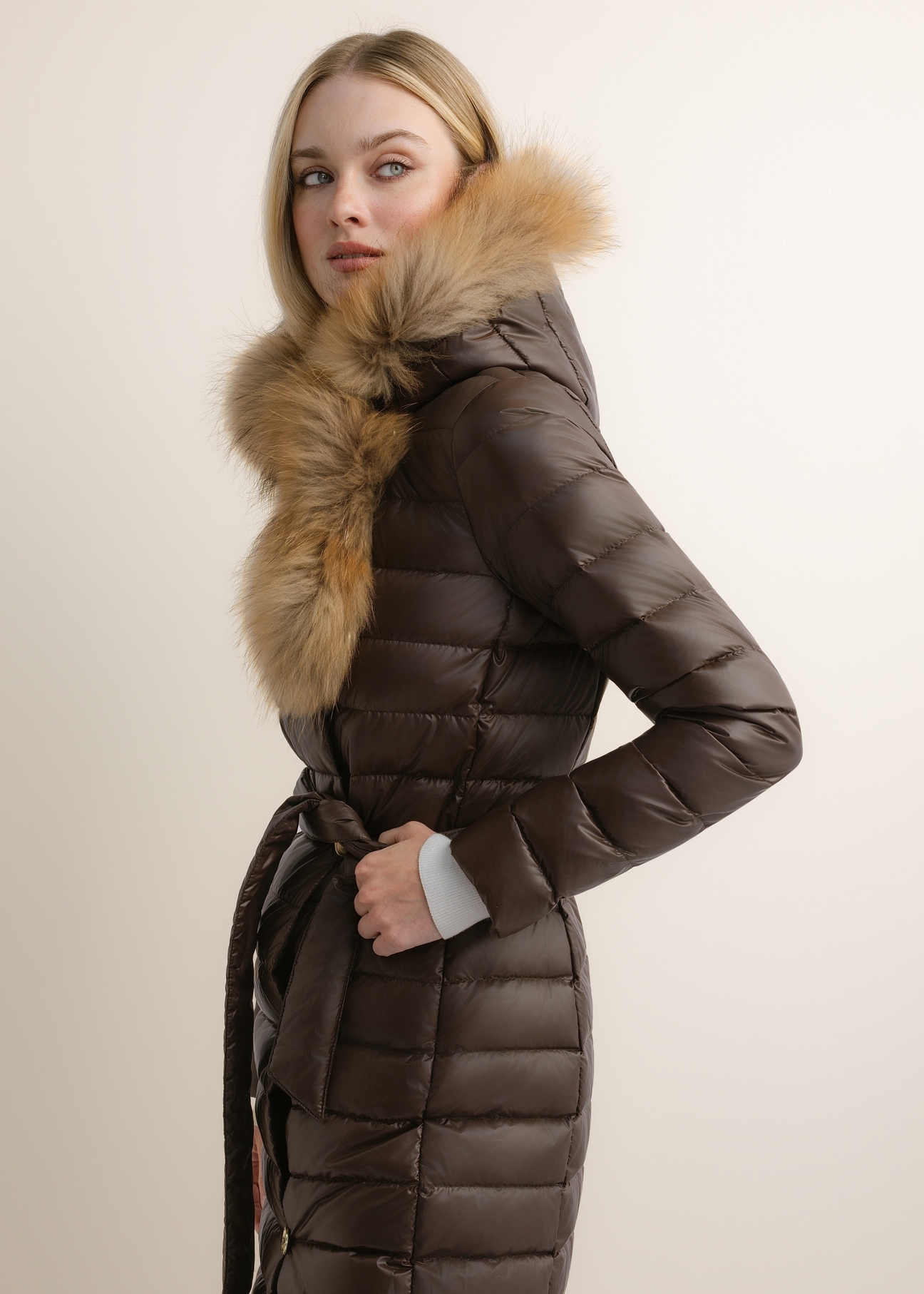 Dark brown long women's jacket with fur KURDT-0706-1I(Z26), side view of the product on the model. Half of the silhouette visible.