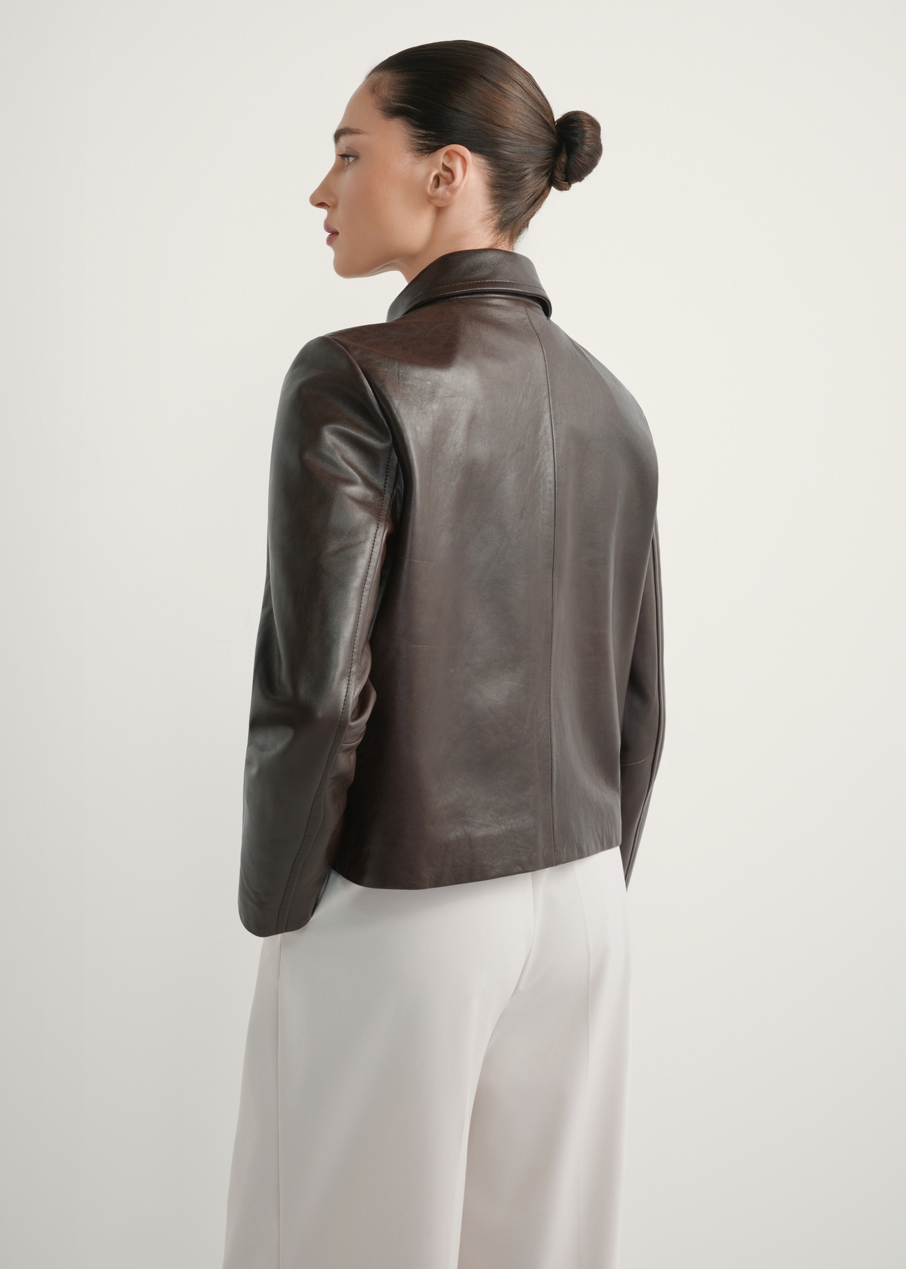 Dark brown women's leather jacket KURDS-0589-1I(W26), back view of the product on the model. Half of the silhouette visible.