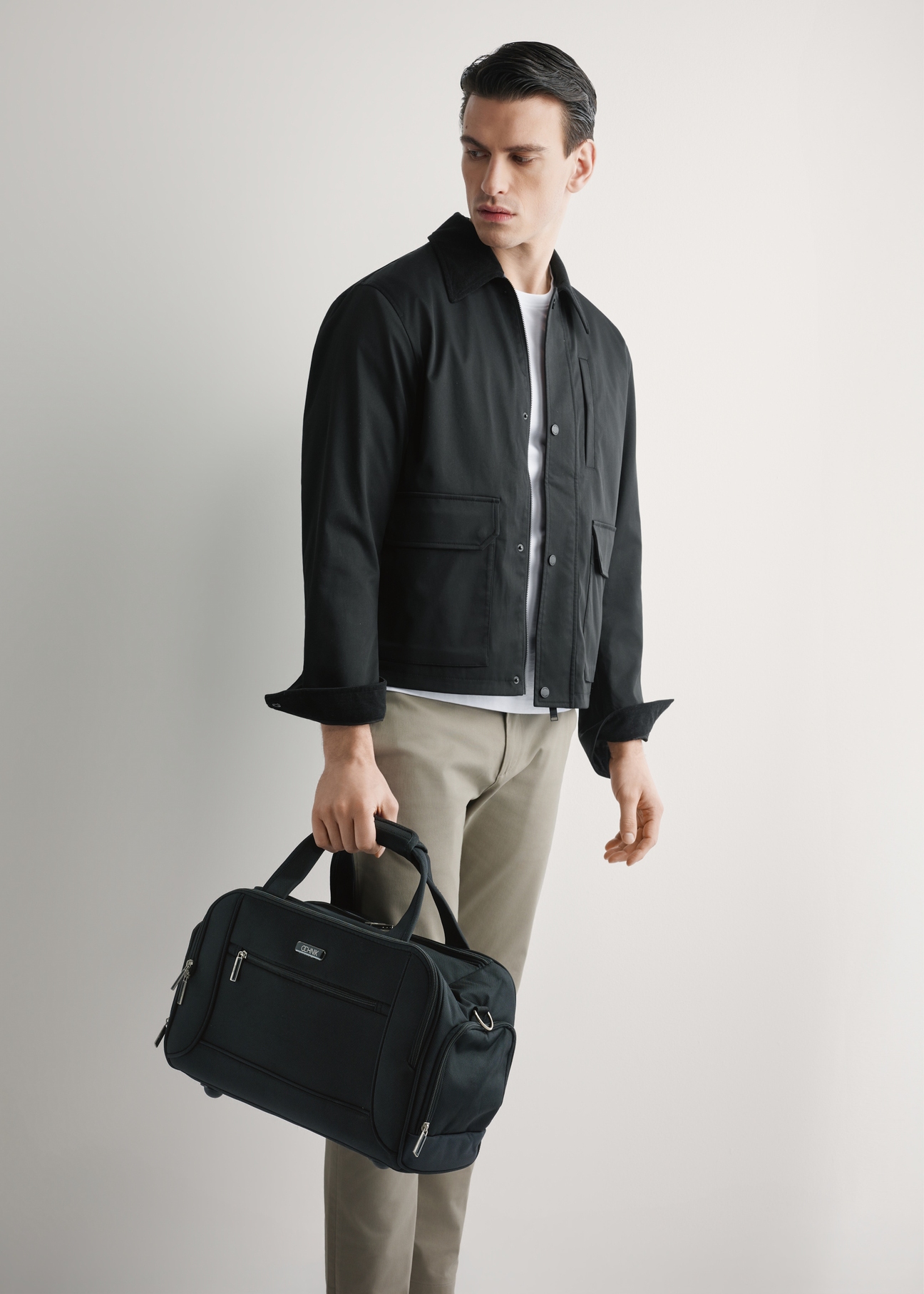 Black men's nylon bag TORMN-0420-99(W26), diagonal view of the product in the model's hand, on a light background.