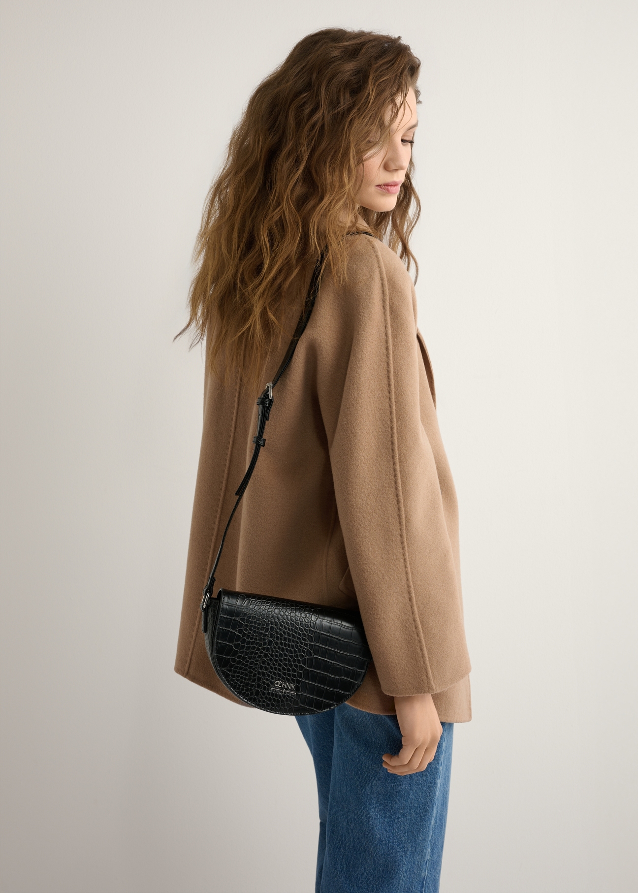 Women's black semi-circular croco messenger bag TOREC-1184-9G(W26), product view on model's shoulder. Half silhouette visible.