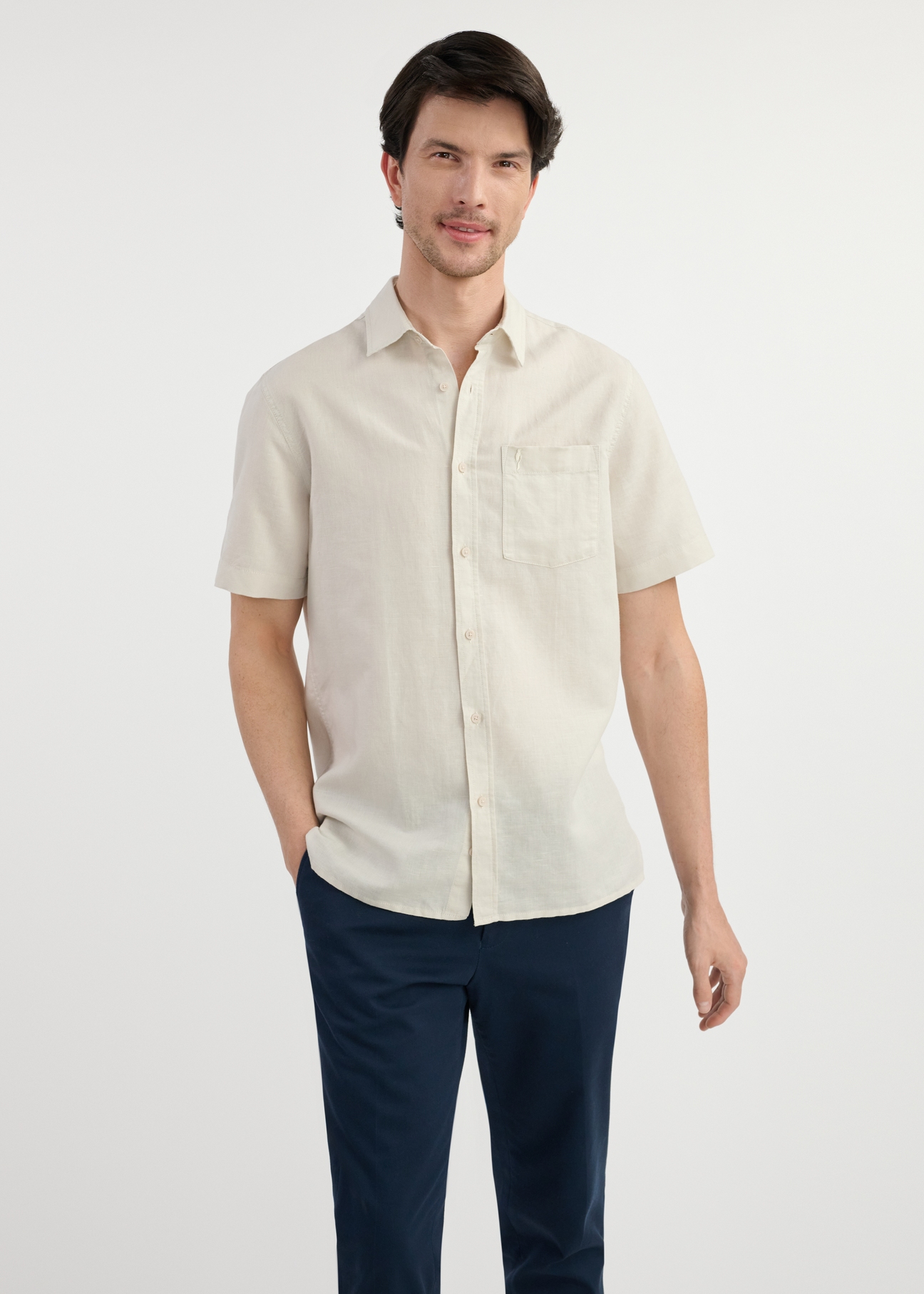 Beige men's shirt with short sleeves KOSMT-0327-81(W25) - front view on the model on a white background. Visible silhouette.
