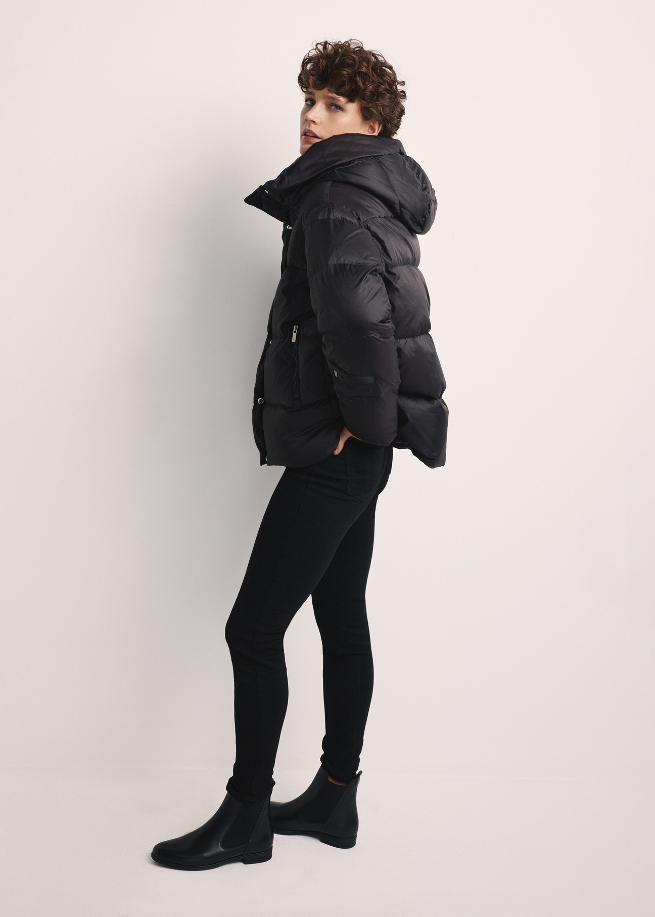Black women's down jacket KURDT-0585-99(Z25), product visible from the side on the model, the entire silhouette is visible.