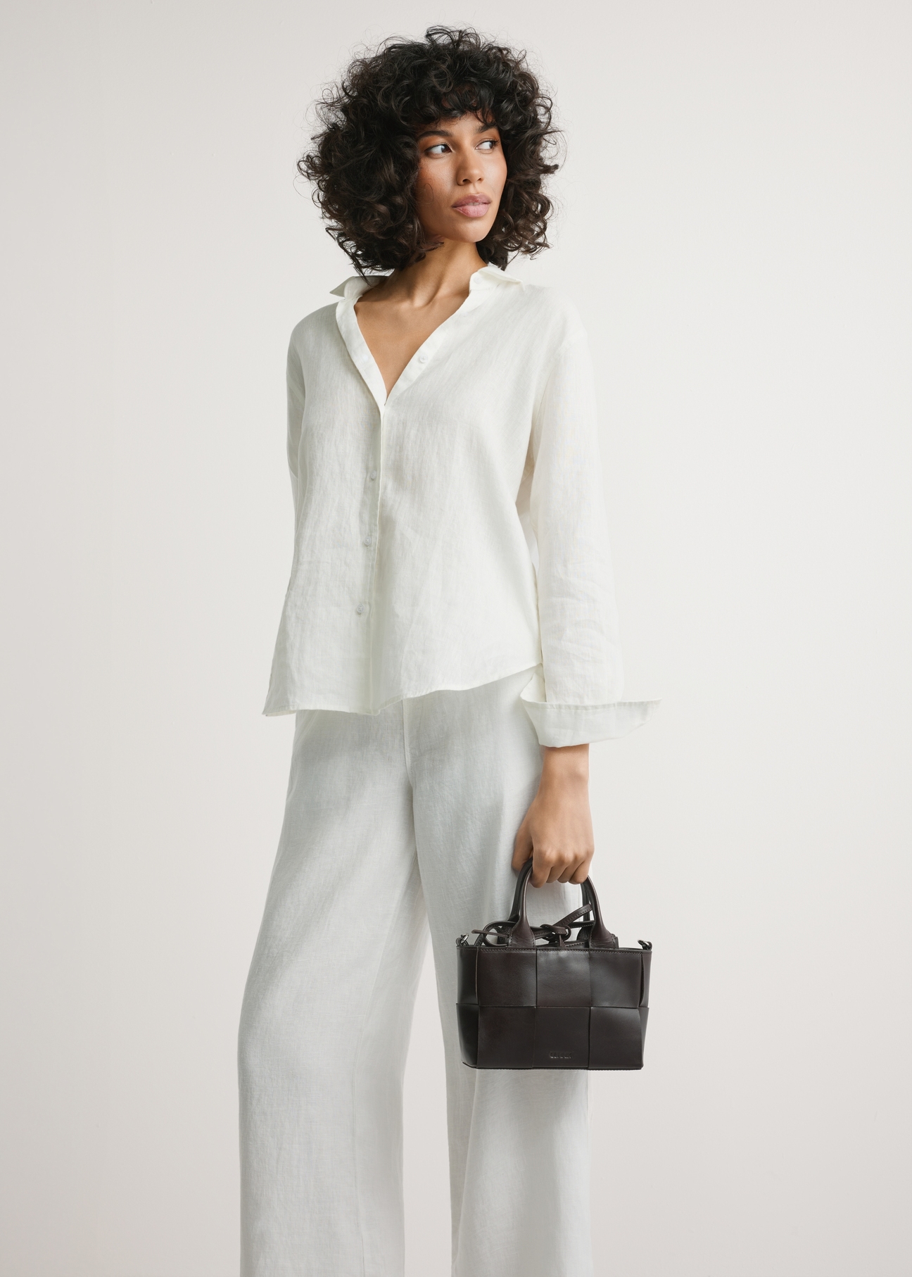 Dark brown small leather women's handbag TORES-1298-1H(W26) - product view, held by a model, against a light background. Knee-length silhouette visible.