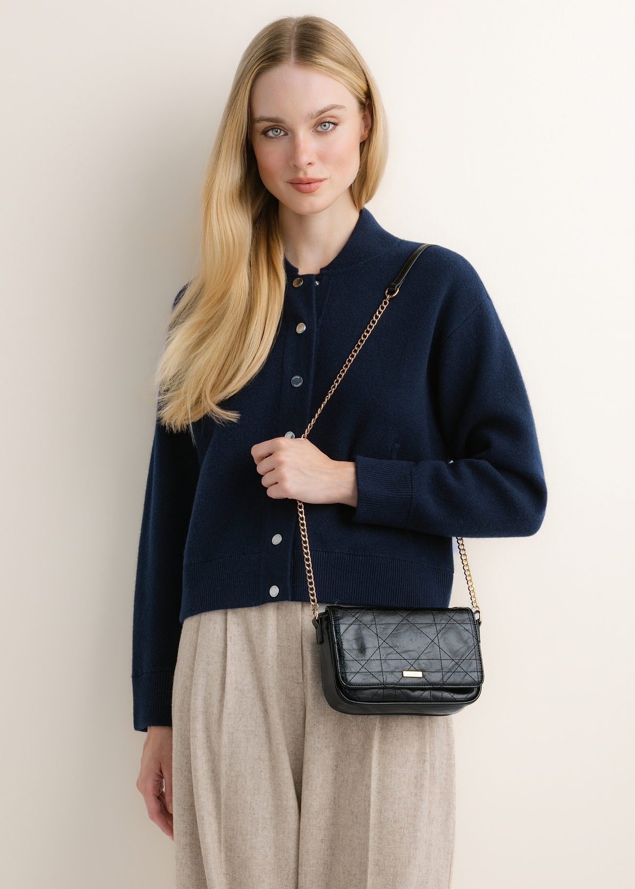 Small black glossy crossbody bag TOREC-1254-9F(Z26); angled view of the product on a model. Half of the figure is visible.