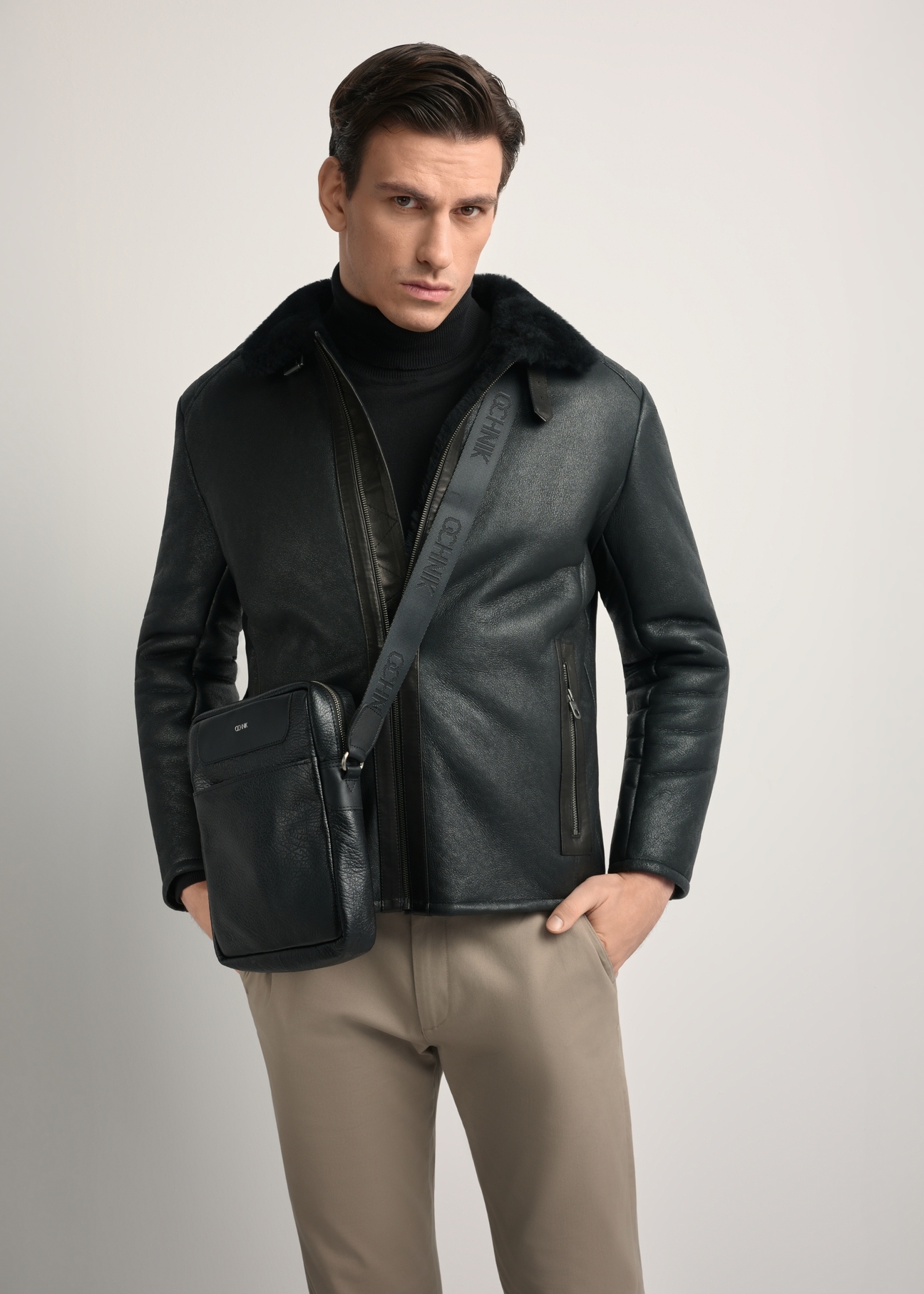 Black leather men's bag with TORMS-0297A-99(Z25) logo - diagonal product view, modeled on a white background. Knee-length silhouette visible.