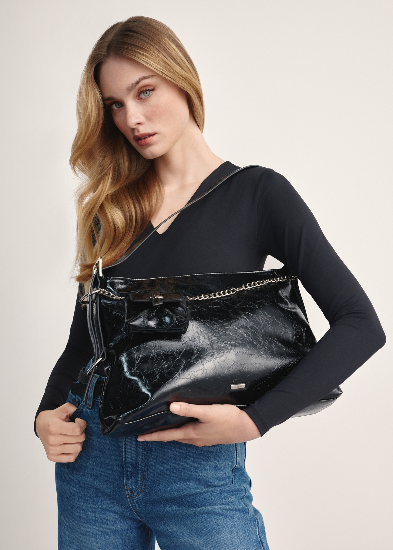 Black patent leather women's handbag TOREC-1073-99(Z25), front view of the product on a model, half of the silhouette visible.