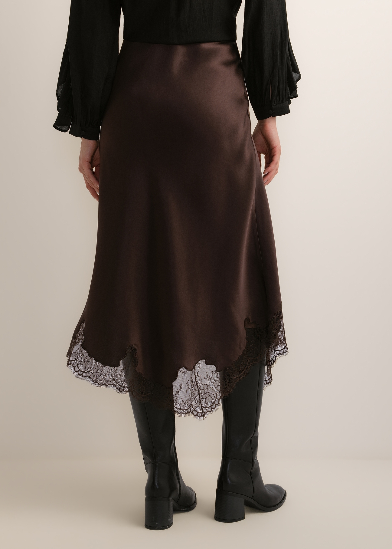 Dark brown asymmetrical women's skirt SPCDT-0135-1I(Z26), product view from the back on the model. Half of the silhouette visible.