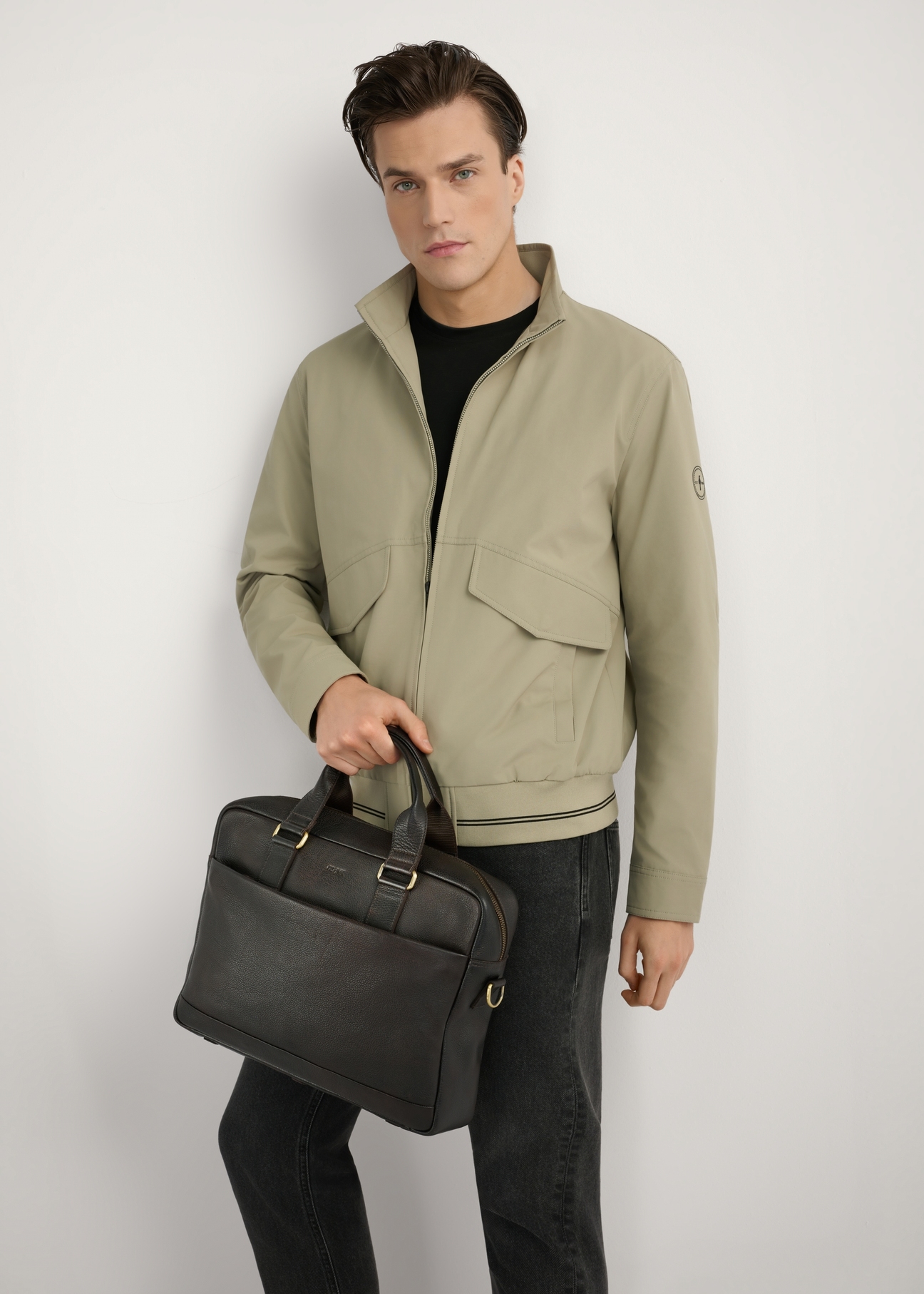 Brown men's leather briefcase TORMS-0503-1I(W26) - front view of the product, held in the model's hand, against a light background, visible silhouette up to the knees.