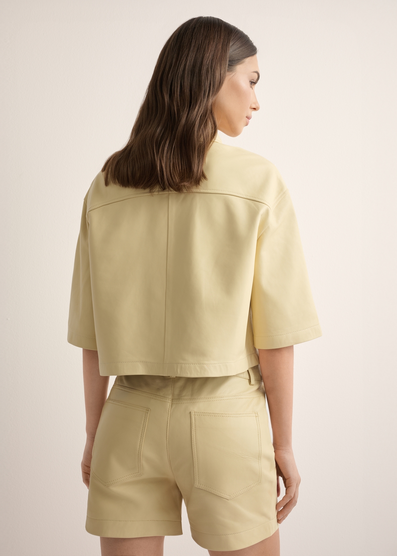 Women's short light yellow leather shirt KOSDS-0005-2A(W26), back view of the product on the model. Half of the silhouette visible.