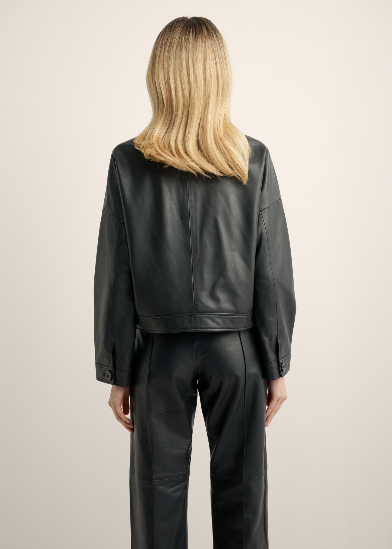 Women's short black leather jacket KURDS-0629-99(Z26), back view of the product on the model. Half of the silhouette visible.
