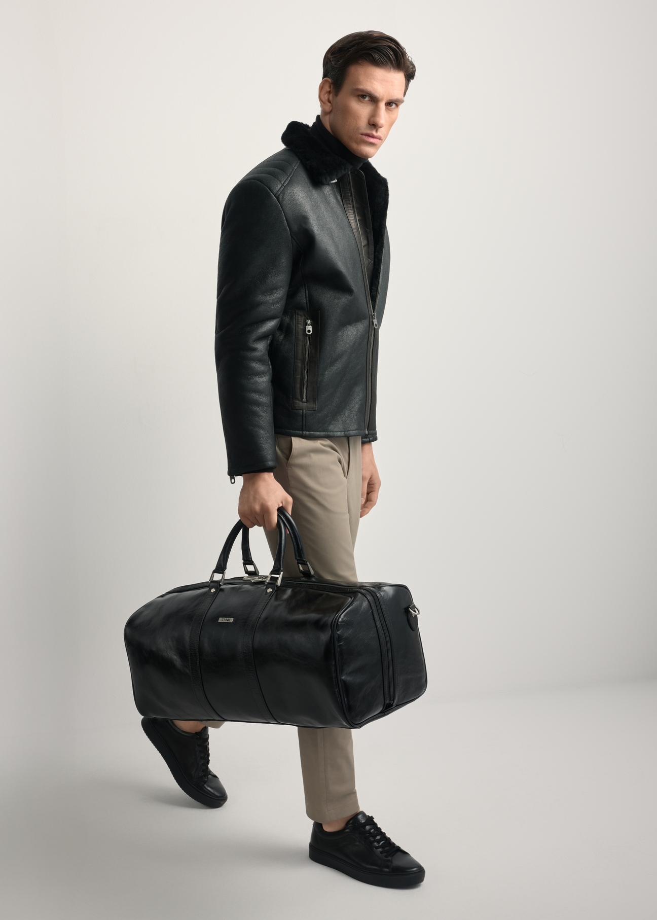 Black leather men's travel bag TORMS-0481-99(Z25) - diagonal view of the product, held by the model. Full body visible.