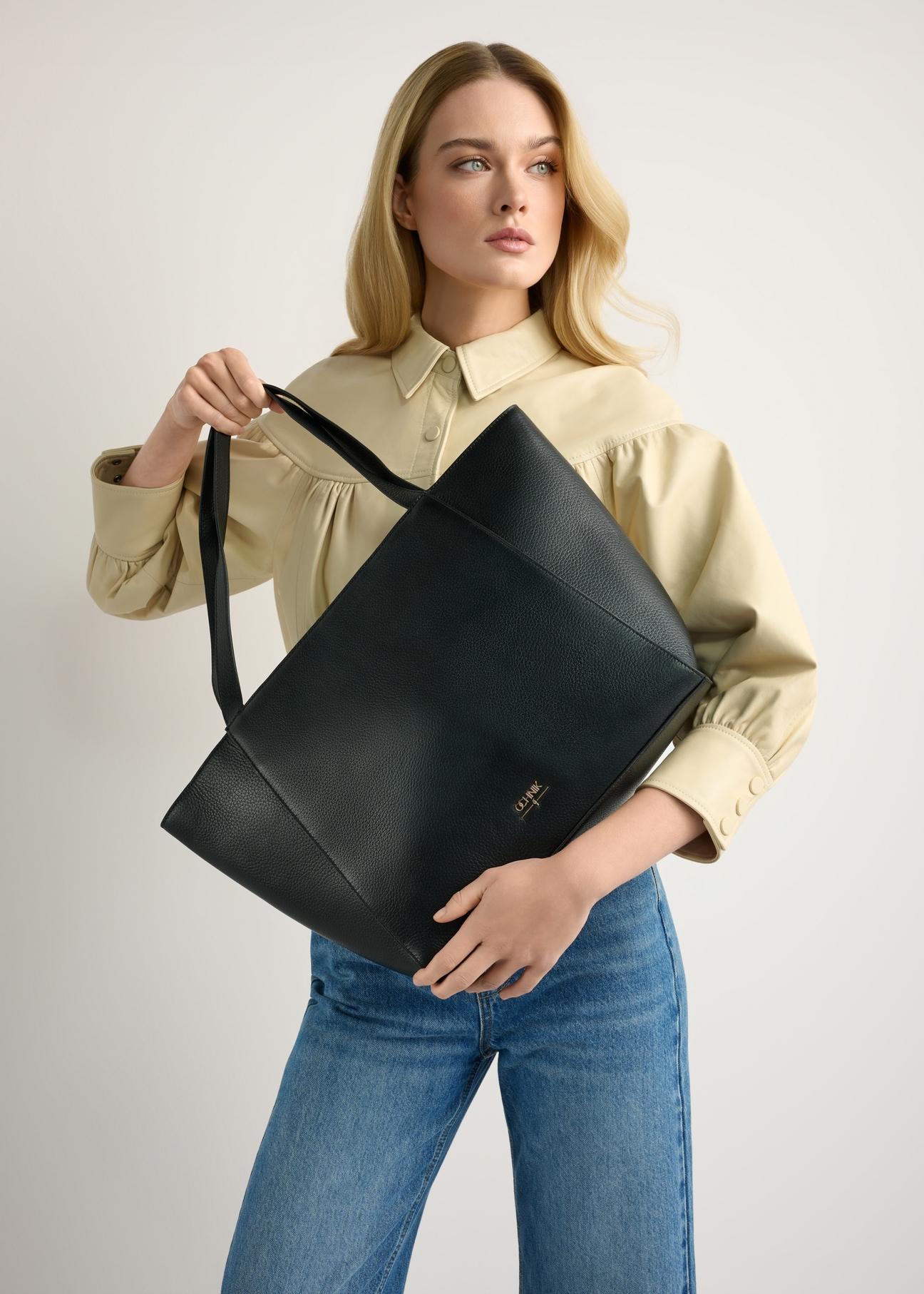 Black leather shopper bag TORES-1209-9I(W26) - front view of the product, held by the model, against a light background. Knee-length silhouette visible.